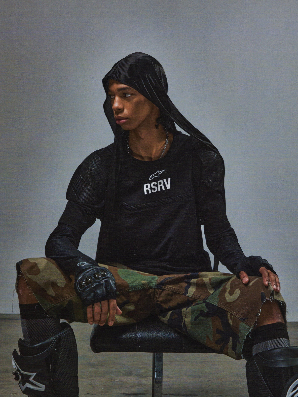 Alpinestars RSRV Nucleon SS Tee, zwart T-shirt met witte RSRV-opdruk, gedragen met camouflagebroek, vingerloos handschoenen en kniebeschermers, urban tactical stijl