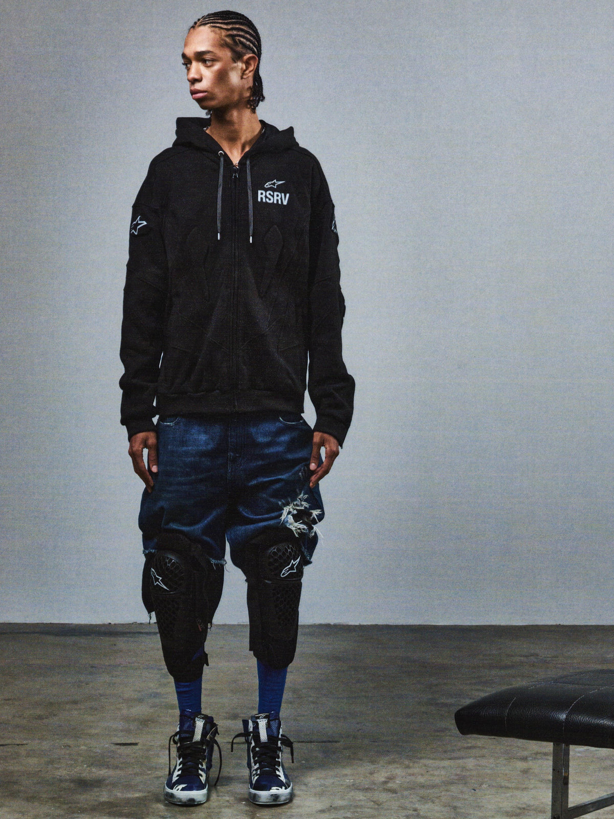 Alpinestars RSRV GP hoodie, zwarte streetwear hoodie met RSRV-logo, gedragen met gescheurde denimshorts en kniebeschermers, casual motorsport-geïnspireerde stijl