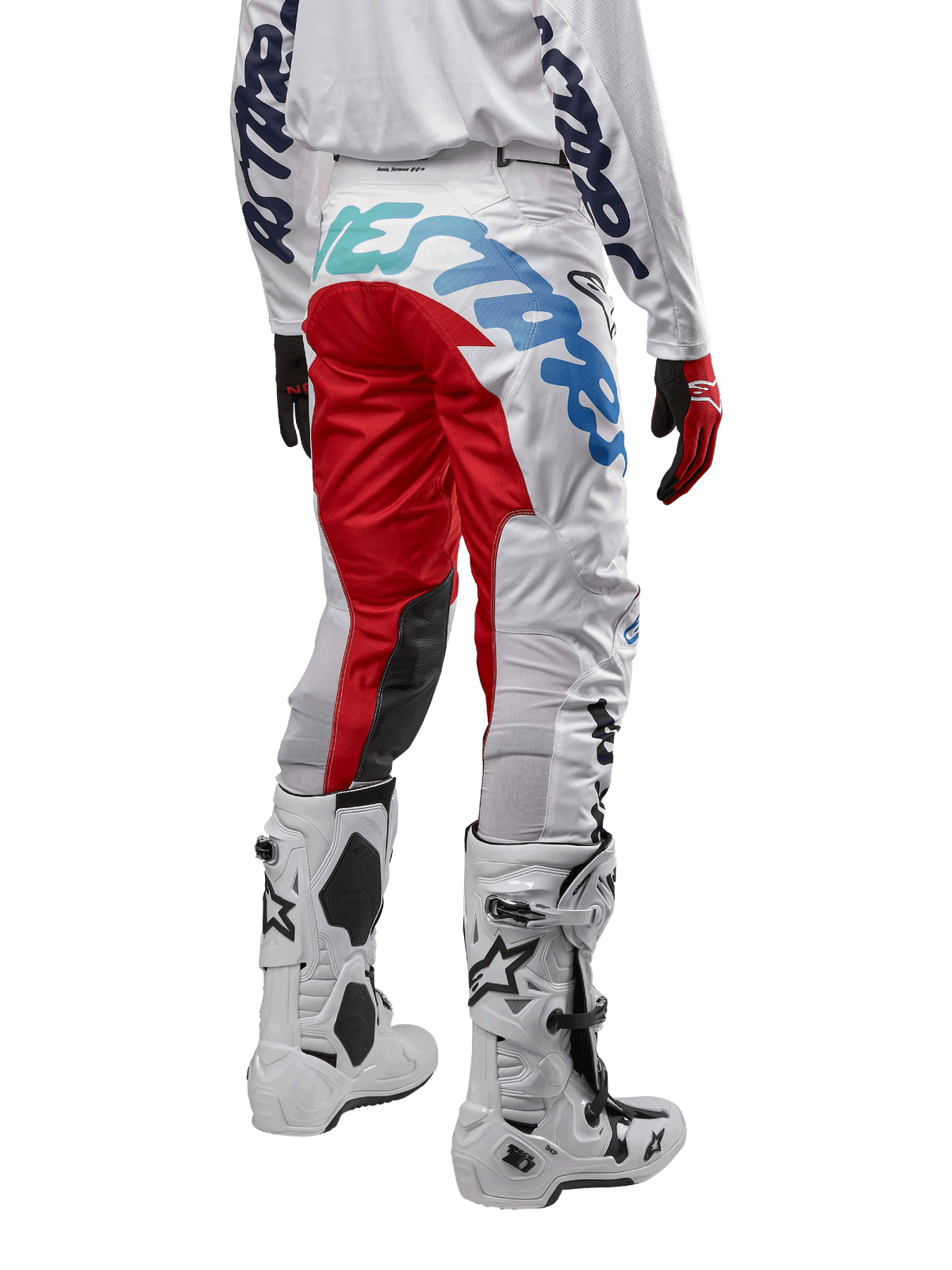 Alpinestars 2024 Racer Hana crossbroek, motorcrossbroek, wit multicolor met rode en blauwe accenten, achteraanzicht met grote branding op het zitvlak, gedragen met wit-zwarte motorcrosslaarzen, ontworpen voor off-road prestaties en duurzaamheid