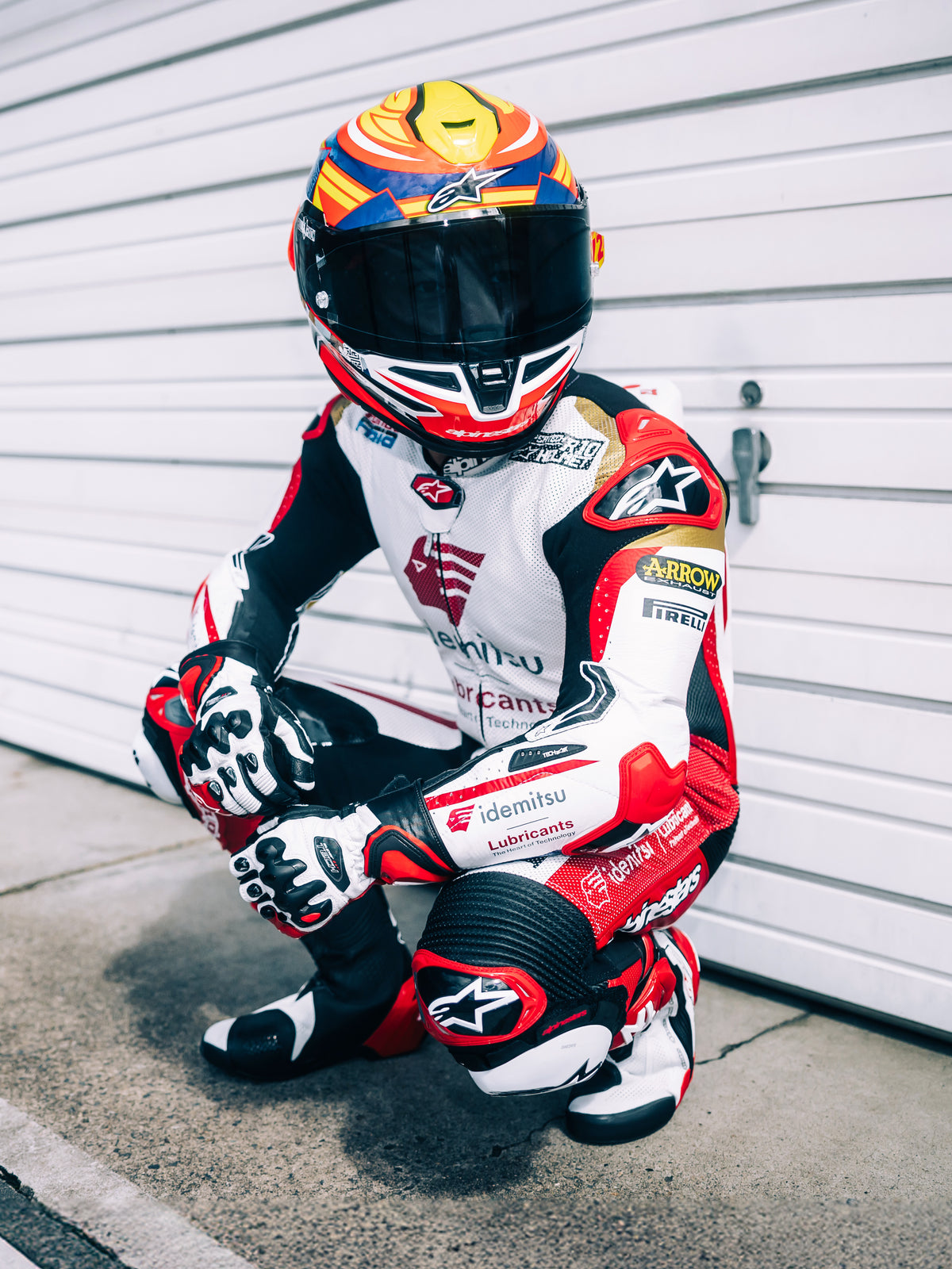 Alpinestars S-R7 Taiyo Furusato helm, integraal motorracehelm, rood, wit, blauw en fluogeel, ECE 22.06-gecertificeerd, gedragen door een motorcoureur in een volledig leren racepak met getint vizier.