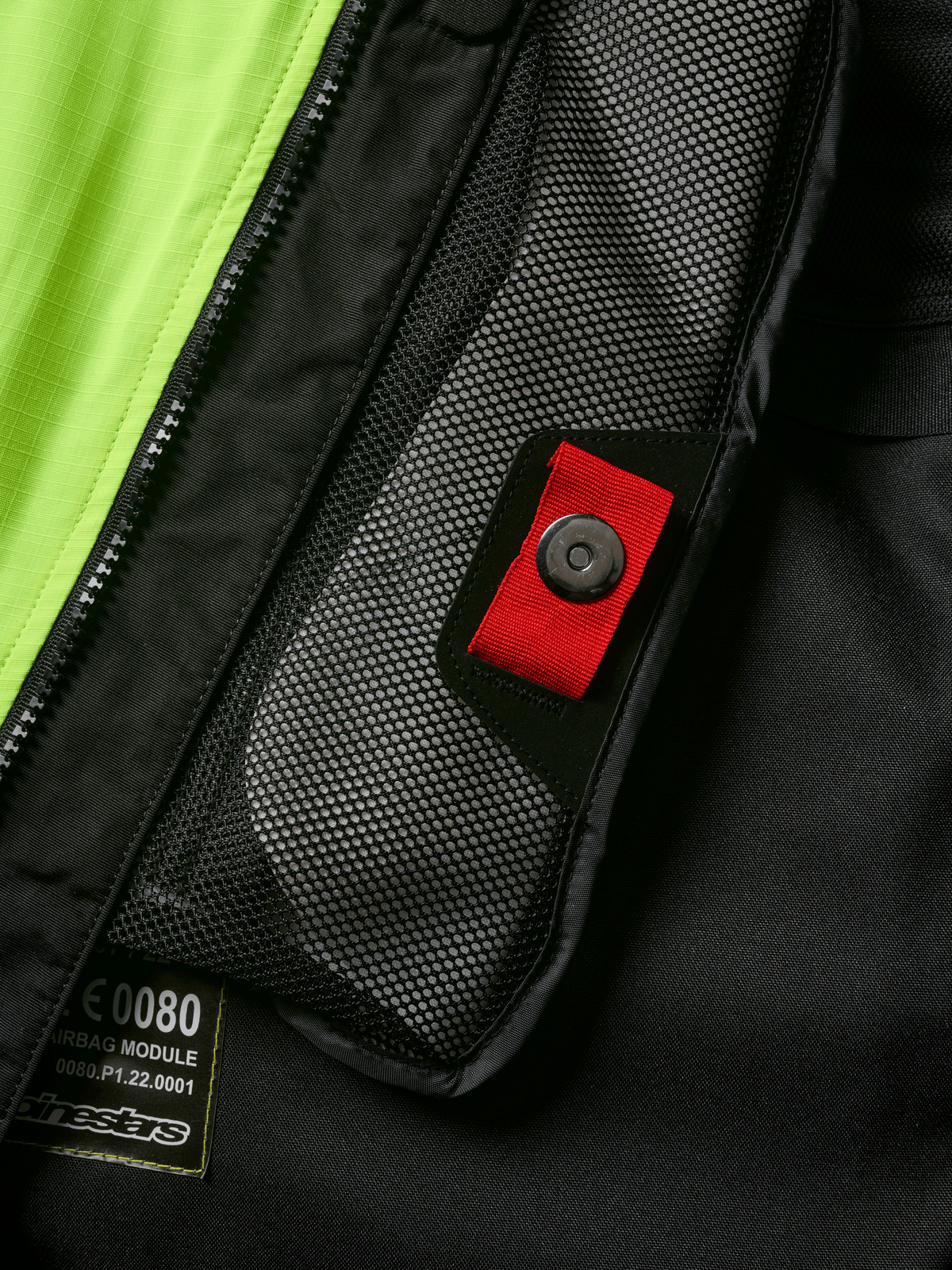 Alpinestars Tech-Air® 3 V2 Systeem detail, close-up van intern meshvak met rood treklipje en druksluiting, opvallend geel fluo paneel, zwarte textiele constructie met airbagmodule-label en rits