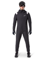 Alpinestars A-Dura Regenjas, mountainbike regenjas, zwart met witte schouderaccenten en wit logo op de borst, gedragen met zwarte broek, zwarte helm, zonnebril en handschoenen, bijpassende mountainbike-uitrusting voor nat weer