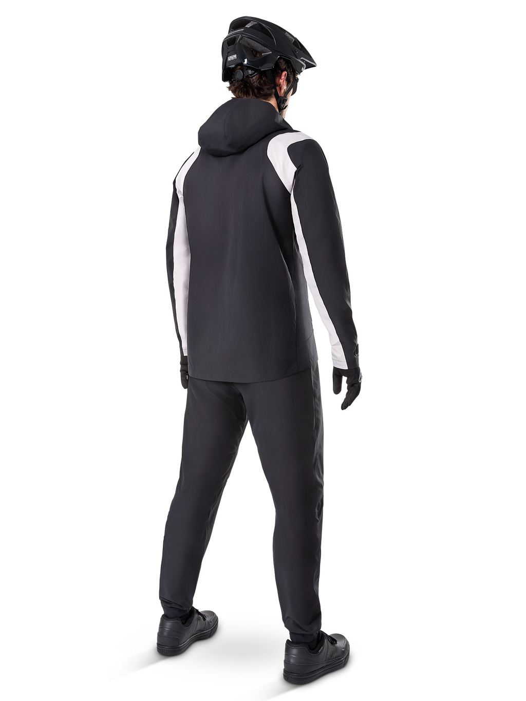 Alpinestars A-Dura Regenjas, achteraanzicht van een mannelijke fietser die het zwart-witte waterdichte MTB-jack draagt, bijpassende zwarte fietsbroek, zwarte helm en handschoenen, technische uitrusting voor mountainbiken in natte omstandigheden.