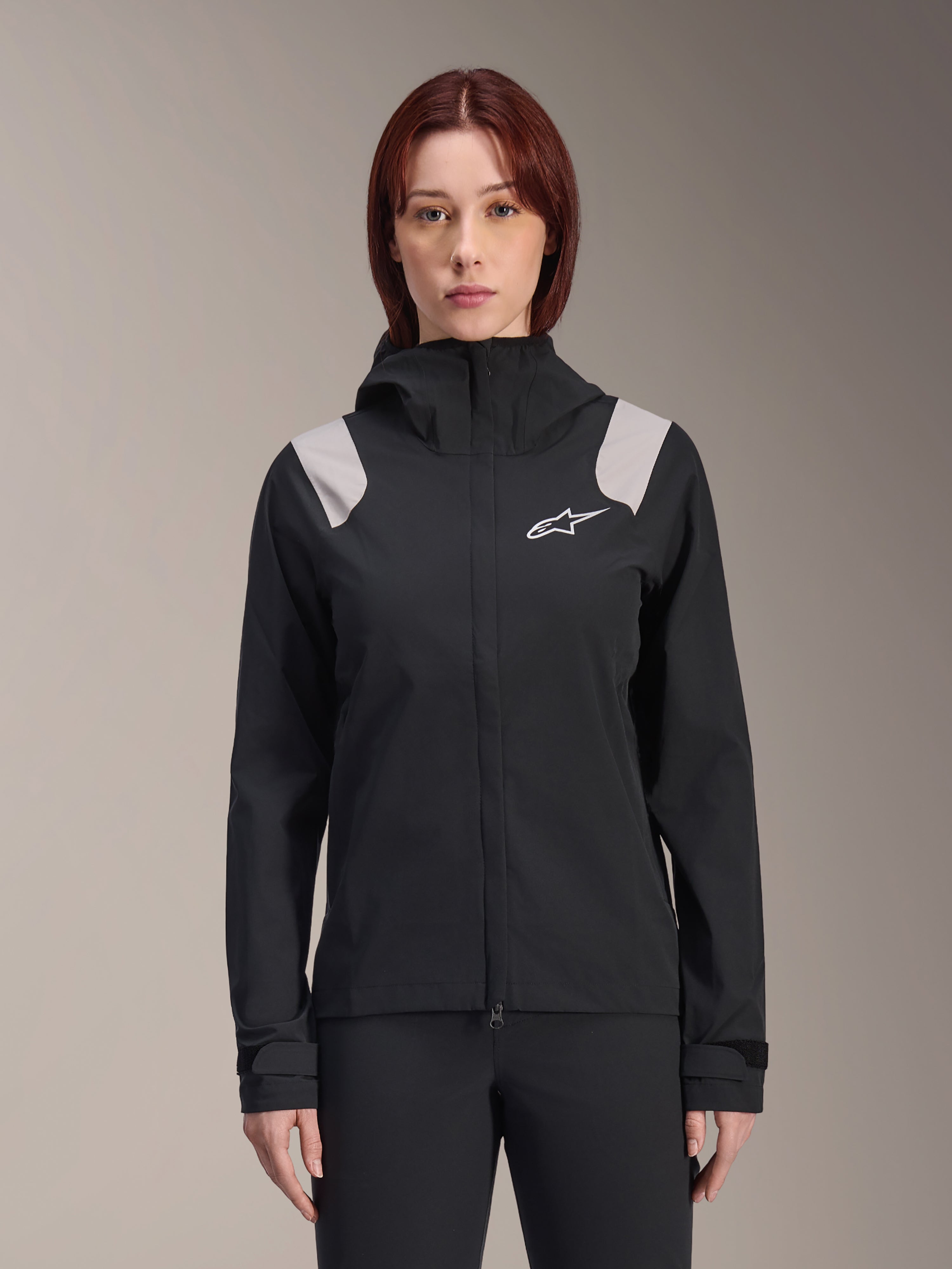 Alpinestars Stella A-Dura regenjas voor dames, MTB-regenjas, zwart met lichtgrijze schouderpanelen, technische shell met capuchon en wit logo op de borst, verstelbare klittenband manchetten, professionele uitrusting voor mountainbiken en rijden in nat weer