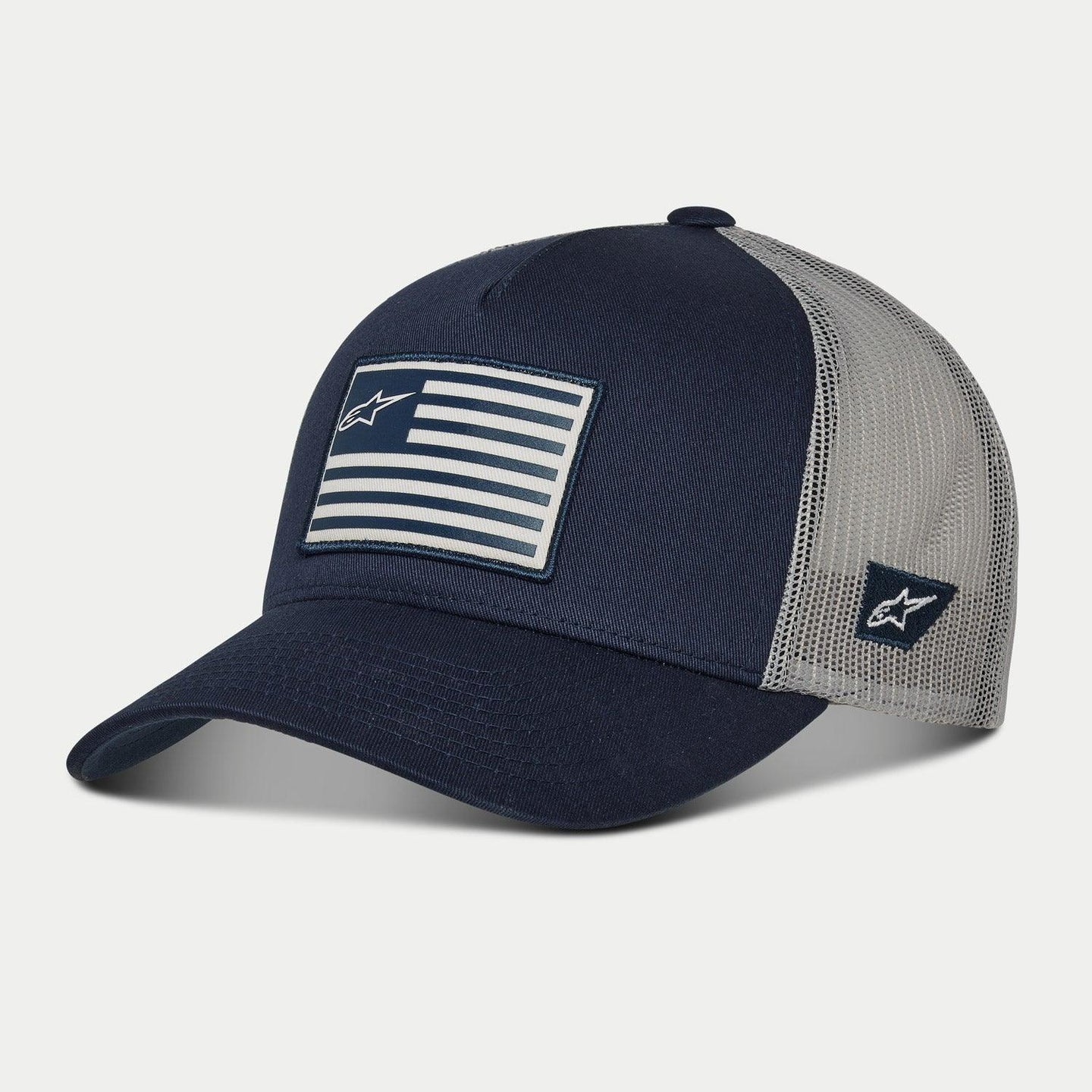 Alpinestars Flag Snapback pet, donkerblauw en grijs, gebogen klep met gestructureerde kroon, bedrukte vlagpatch op de voorkant en geborduurd logo aan de zijkant, mesh achterkant voor ventilatie, casual motorsport-geïnspireerde pet