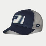 Alpinestars Flag Snapback pet, donkerblauw en grijs, gebogen klep met gestructureerde kroon, bedrukte vlagpatch op de voorkant en geborduurd logo aan de zijkant, mesh achterkant voor ventilatie, casual motorsport-geïnspireerde pet