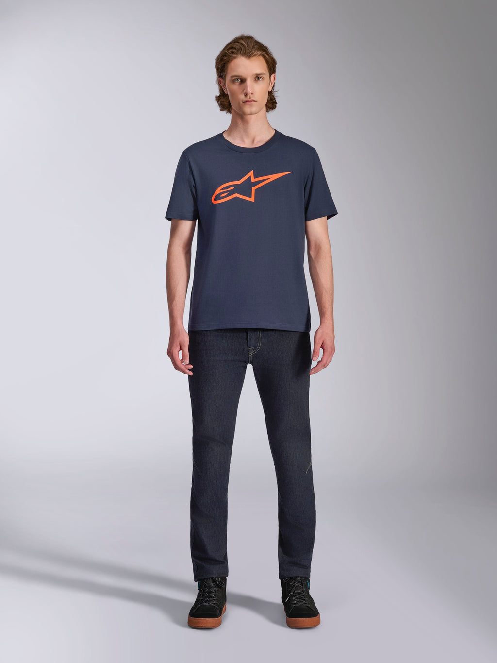 Alpinestars Ageless 2.0 CSF Tee, T-shirt met korte mouwen, donkerblauw met oranje Alpinestars-logo, gedragen door model met donkere jeans en sneakers, casual motorsport streetwear