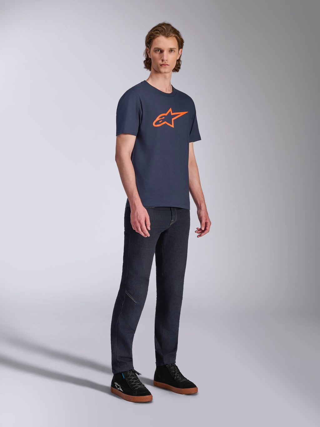 Alpinestars Ageless 2.0 CSF Tee, T-shirt met korte mouwen, marineblauw met oranje ster-logo, gedragen met donkere denim jeans en zwarte sneakers, casual motorsport-geïnspireerde streetwear