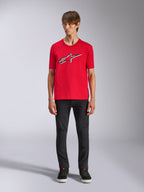 Alpinestars Ageless Shadow CSF Tee, T-shirt met korte mouwen, rood, Ageless-logo op de voorzijde met witte en zwarte contouren, gedragen door een model met zwarte broek en sneakers, casual motorsport streetwear