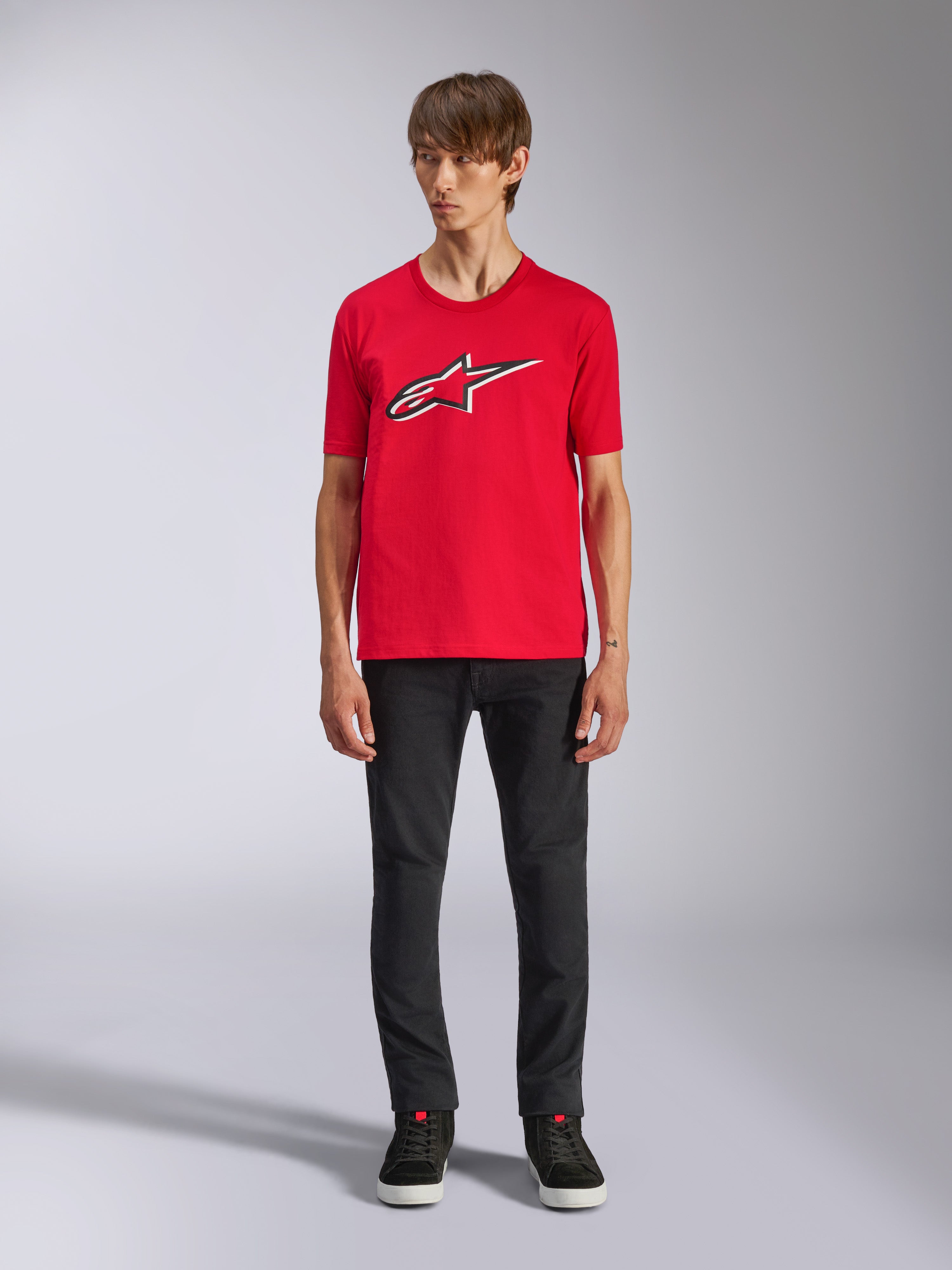 Alpinestars Ageless Shadow CSF Tee, T-shirt met korte mouwen, rood, Ageless-logo op de voorzijde met witte en zwarte contouren, gedragen door een model met zwarte broek en sneakers, casual motorsport streetwear