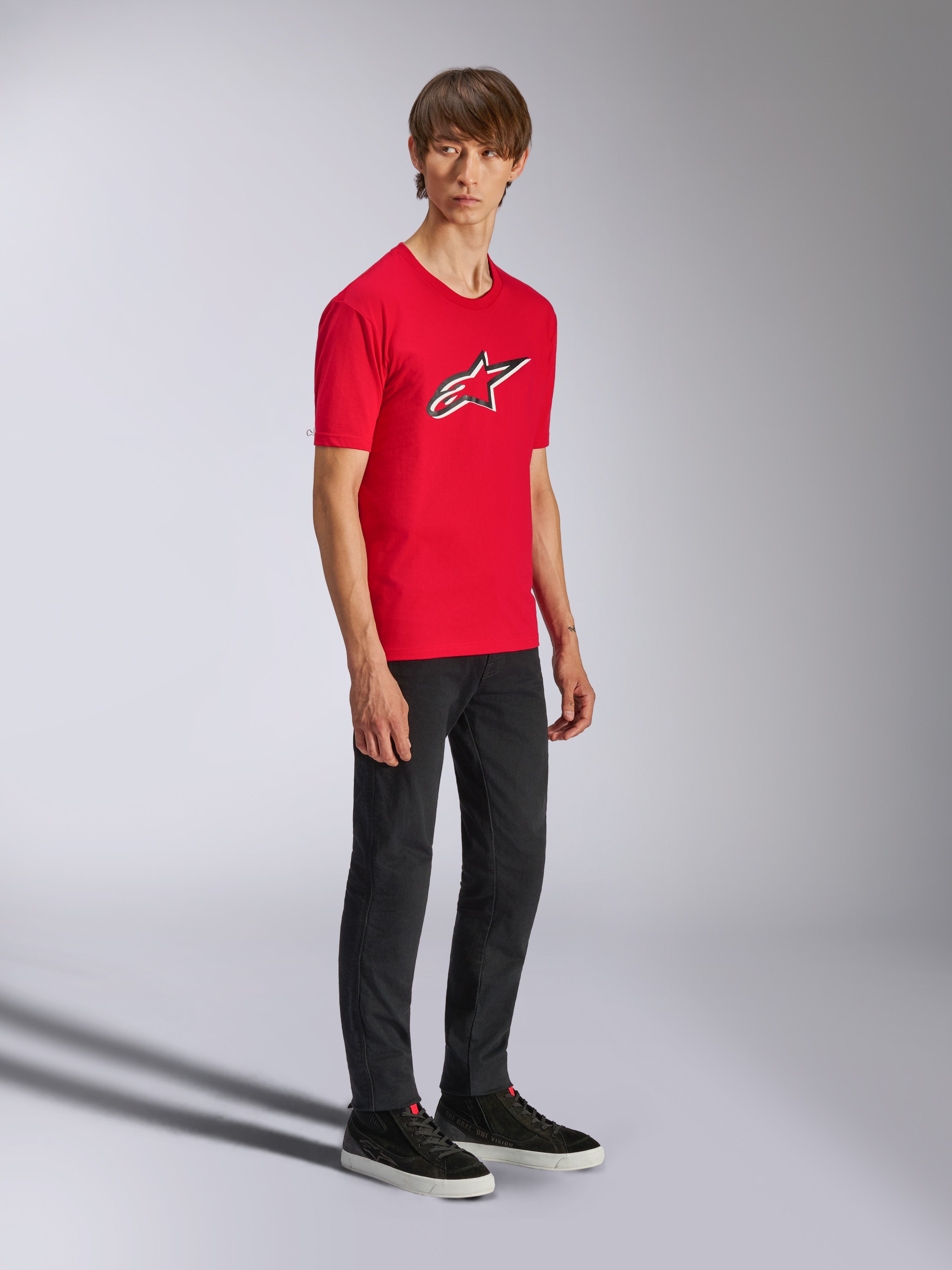 Alpinestars Ageless Shadow CSF Tee, rood T-shirt met korte mouwen, met een groot Ageless-logo op de borst, gedragen door een model met zwarte broek en sneakers, casual motorsport streetwear