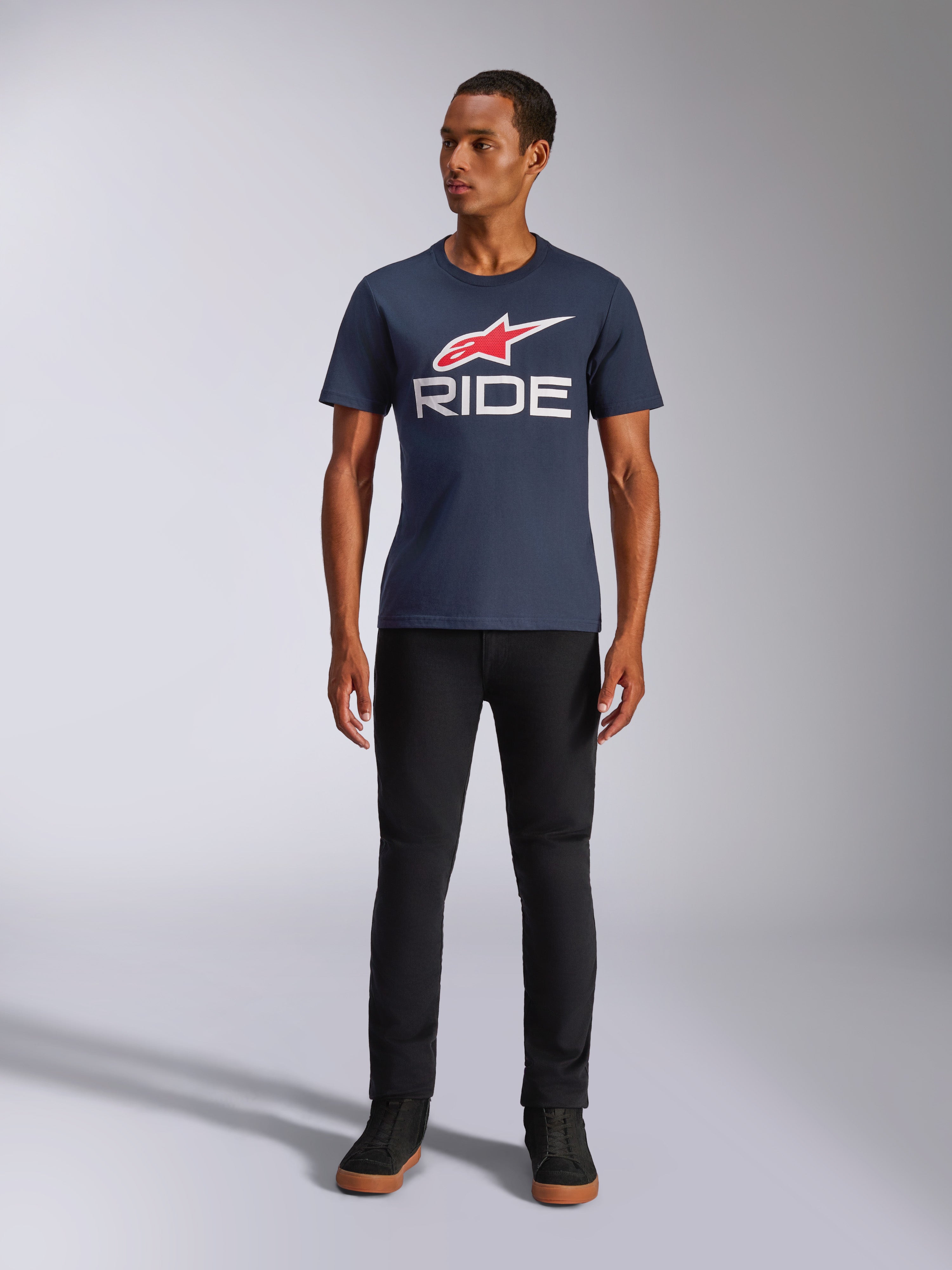 Alpinestars Ride 4.0 CSF Tee, T-shirt met korte mouwen, donkerblauw met rood Alpinestars sterlogo en witte 'RIDE' tekst op de borst, gedragen door model met zwarte broek en zwarte sneakers, casual op motorsport geïnspireerde streetwear