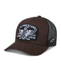 Alpinestars Heritage Patch Trucker Pet, bruin en zwart, met een grote patch aan de voorkant met geborduurd gevleugeld wiel en de tekst 'RACING AHEAD EST. 1963', ademende zwarte mesh achterkant, gebogen klep, wit sterlogo aan de zijkant, op motorsport geïnspireerde casual pet