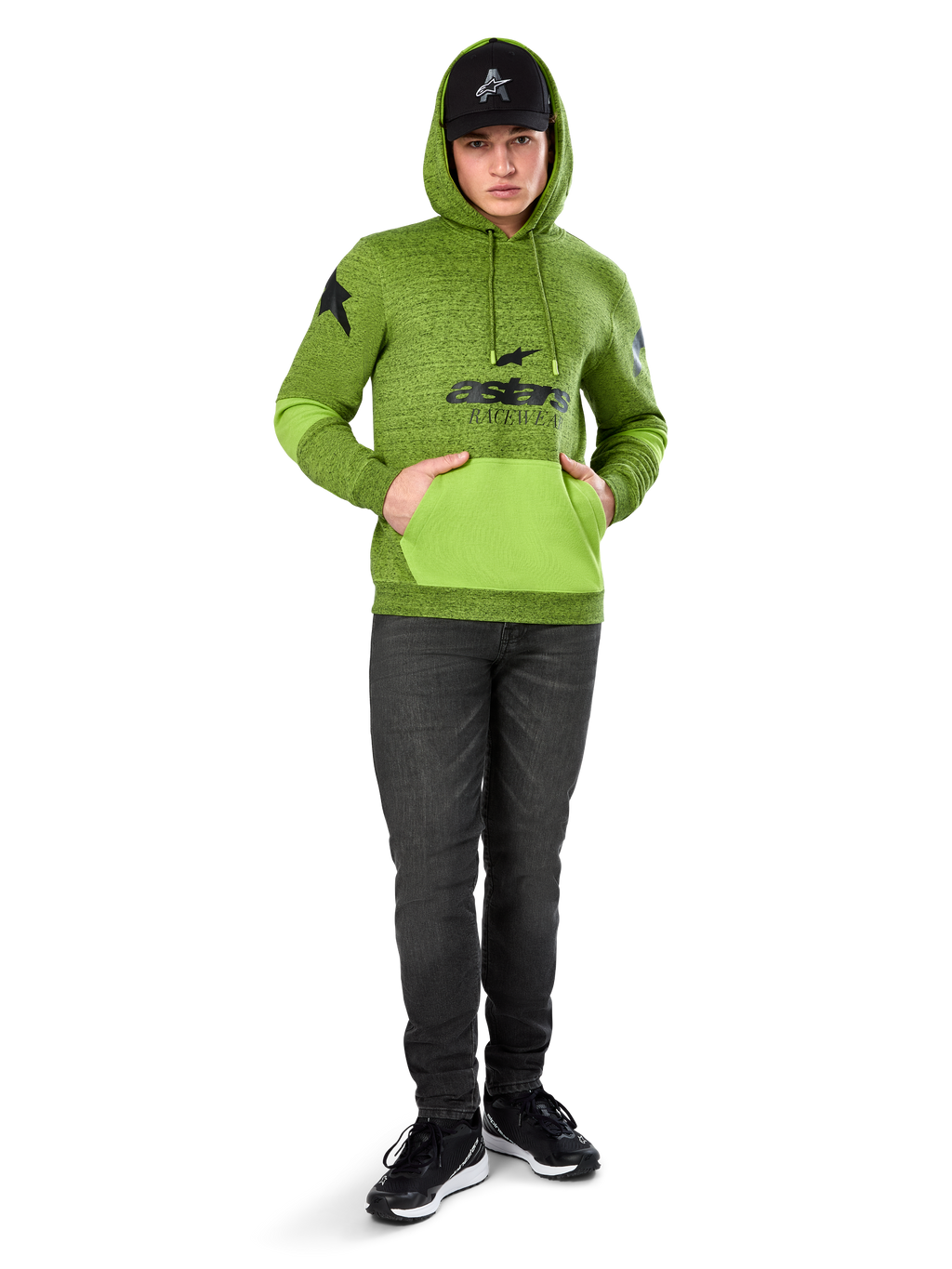 Alpinestars Perpetuate Hoodie, gemêleerde limegroene pullover fleece met contrasterende felgroene kangoeroezak en mouwpanelen, zwarte 'astars' graphic op de voorzijde, gedragen met een zwarte pet en donkere jeans, casual motorsport-geïnspireerde streetwear