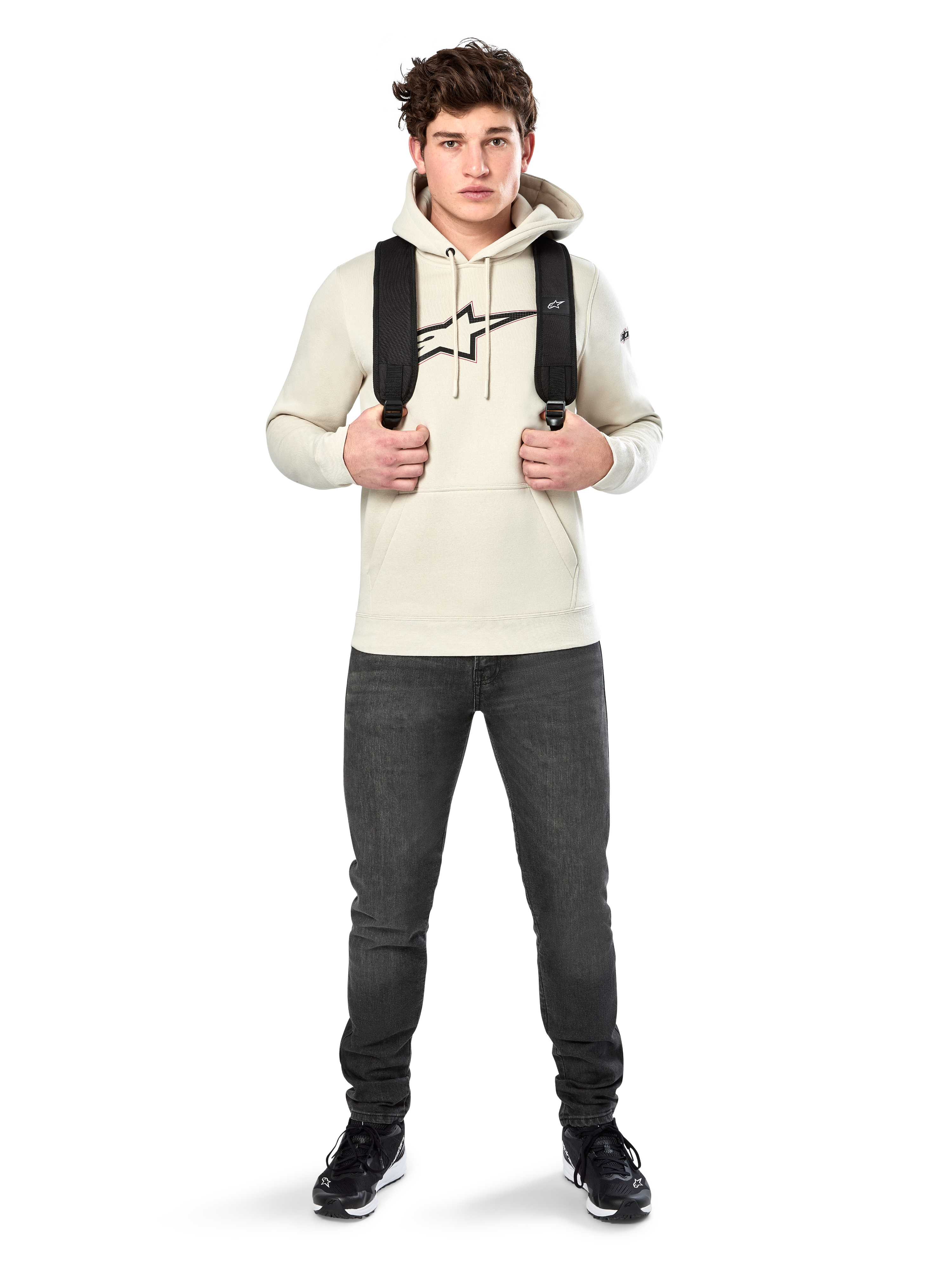 Alpinestars Insignia Hoodie, casual streetwear, Off White fleece pullover, logo met carbonlook en rode omtrek, capuchon met trekkoord, kangoeroezak, gedragen door model met zwarte rugzak en donkergrijze jeans