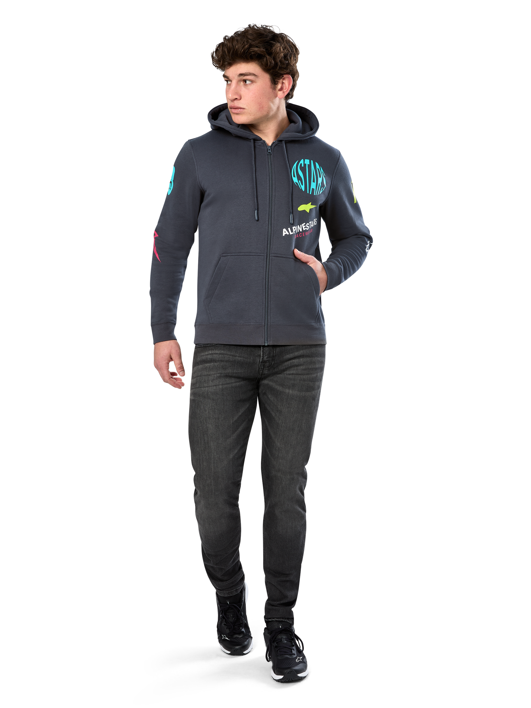 Alpinestars Variegate Hoodie, zip-front fleece hoodie, Gunmetal gray, worn by model with black jeans and sneakers, featuring teal 'ASTARS' branding and colorful logo art on sleeves and chest, casual motorsport-inspired streetwear