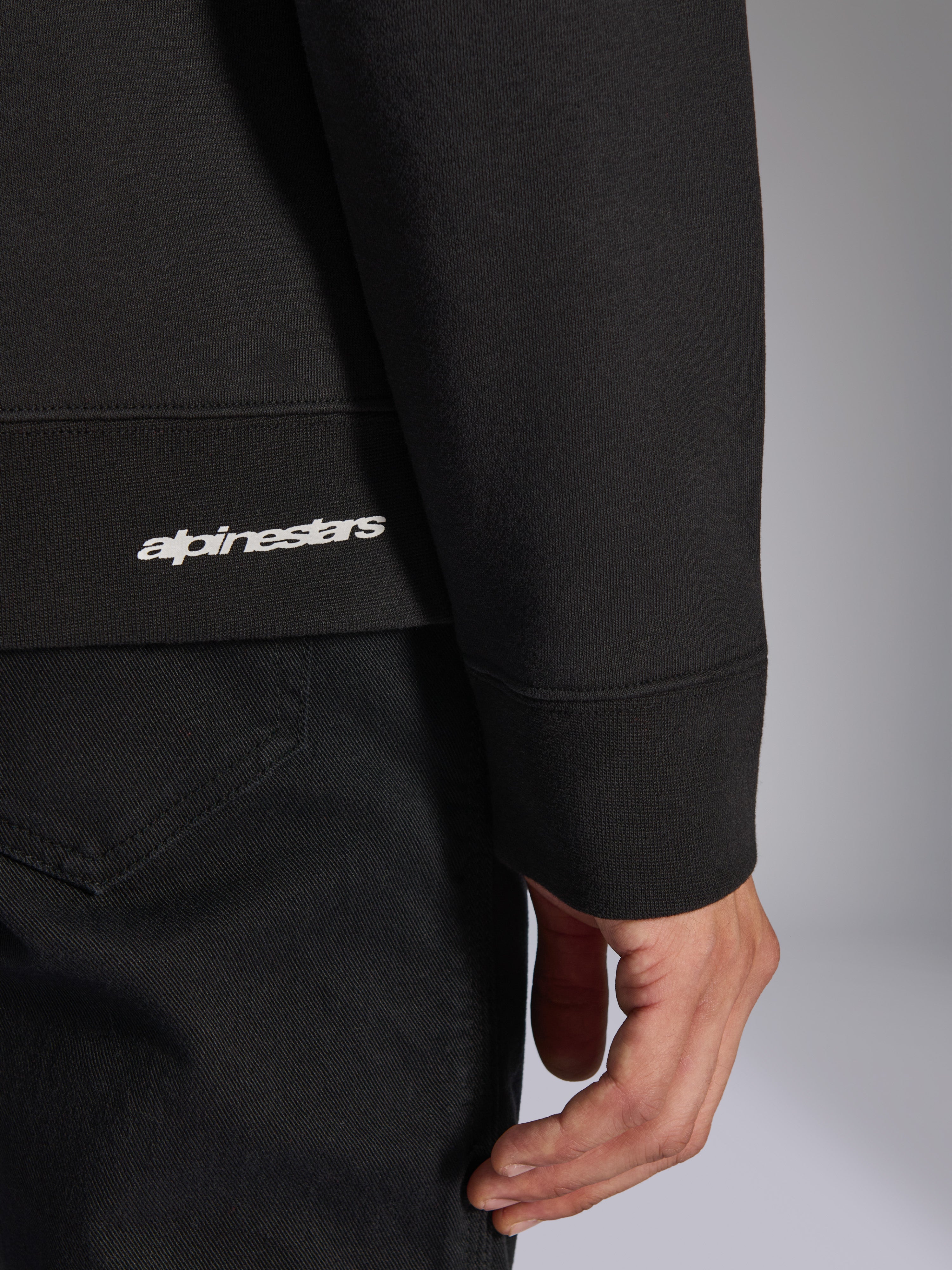 Alpinestars Positive Crew, zwarte pullover sweatshirt, detailopname van de geribbelde zoom en mouwboord met wit Alpinestars-logo, hoogwaardige stoftextuur, casual op motorsport geïnspireerde sportkleding