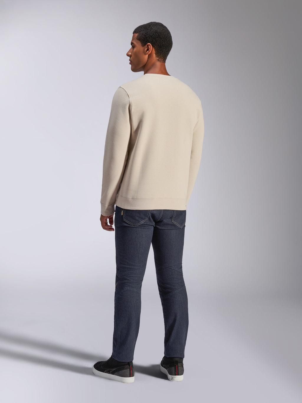 Alpinestars Positive Crew, Off White sweatshirt met ronde hals, achteraanzicht op model, gecombineerd met een donkere denim jeans en zwarte sneakers, casual motorsport streetwear, met geribde boorden en zoom