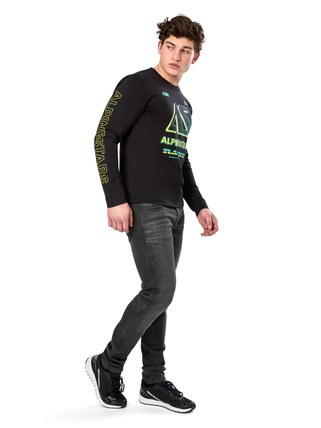 Alpinestars Ayess CSF shirt met lange mouwen, zwart, voorzien van gele belettering op de mouw en opvallende limoengroene en cyaanblauwe borstgraphics, gecombineerd met een donkergrijze jeans en zwarte sneakers, casual motorsport-geïnspireerde streetwear.