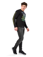 Alpinestars Ayess CSF shirt met lange mouwen, zwart, voorzien van gele belettering op de mouw en opvallende limoengroene en cyaanblauwe borstgraphics, gecombineerd met een donkergrijze jeans en zwarte sneakers, casual motorsport-geïnspireerde streetwear.