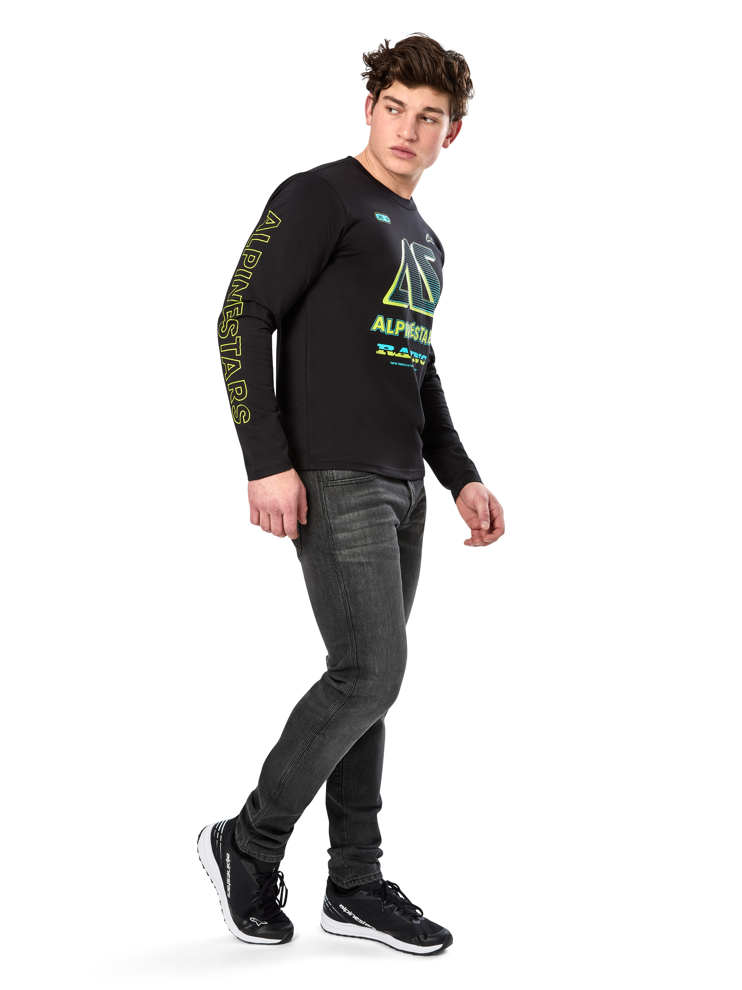 Alpinestars Ayess CSF shirt met lange mouwen, zwart, voorzien van gele belettering op de mouw en opvallende limoengroene en cyaanblauwe borstgraphics, gecombineerd met een donkergrijze jeans en zwarte sneakers, casual motorsport-geïnspireerde streetwear.
