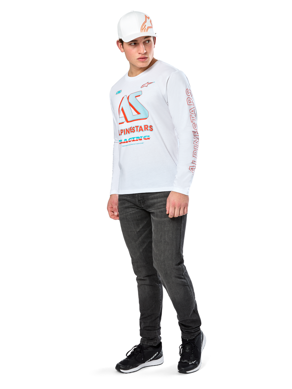 Alpinestars Ayess CSF Tee, T-shirt met lange mouwen, wit, met grote blauwe en rode CSF racing graphics op de borst en rode Alpinestars-branding op de mouw, gedragen met een donkere jeans en een witte Alpinestars pet, casual motorsport streetwear