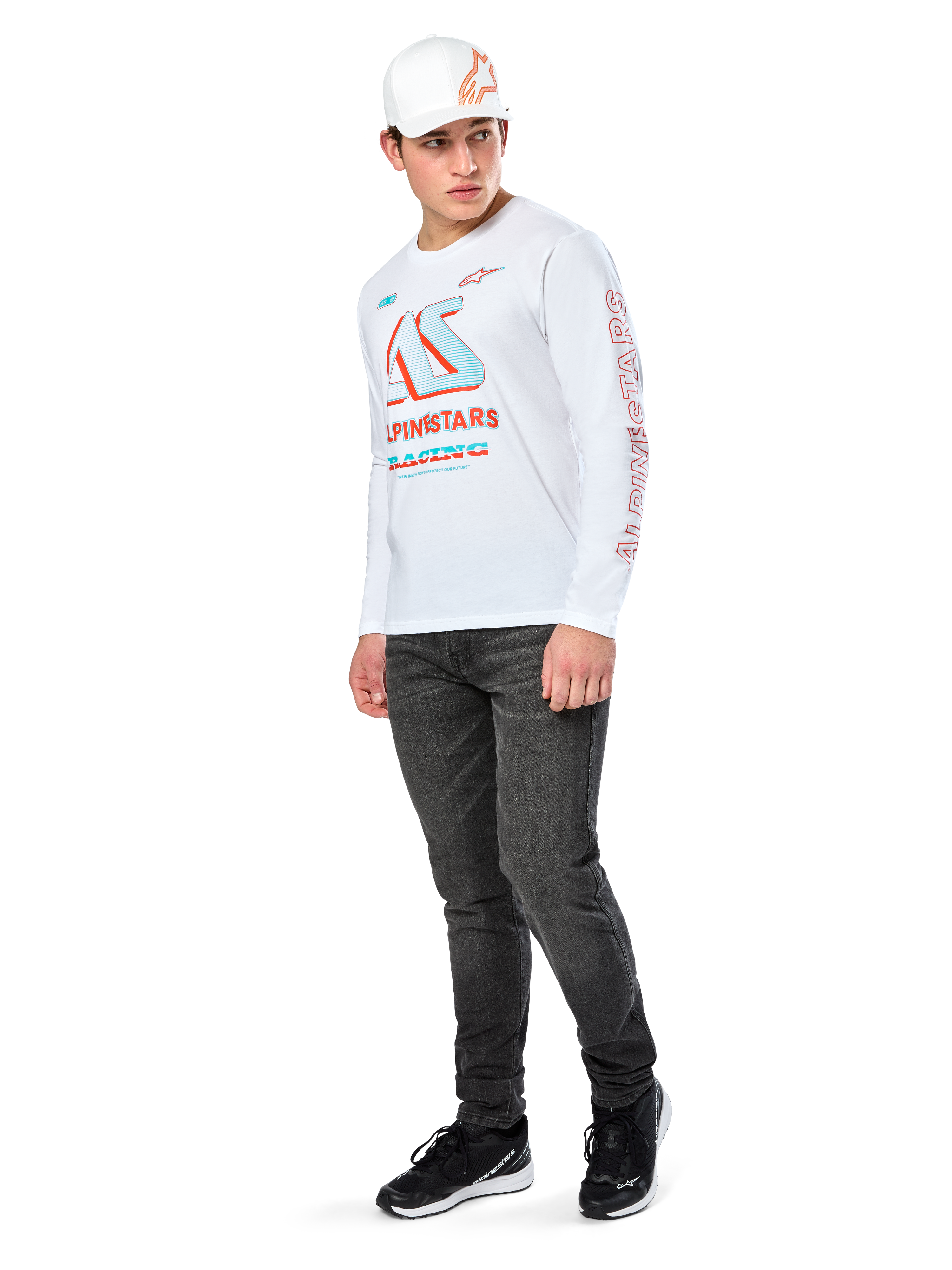 Alpinestars Ayess CSF Tee, T-shirt met lange mouwen, wit, met grote blauwe en rode CSF racing graphics op de borst en rode Alpinestars-branding op de mouw, gedragen met een donkere jeans en een witte Alpinestars pet, casual motorsport streetwear