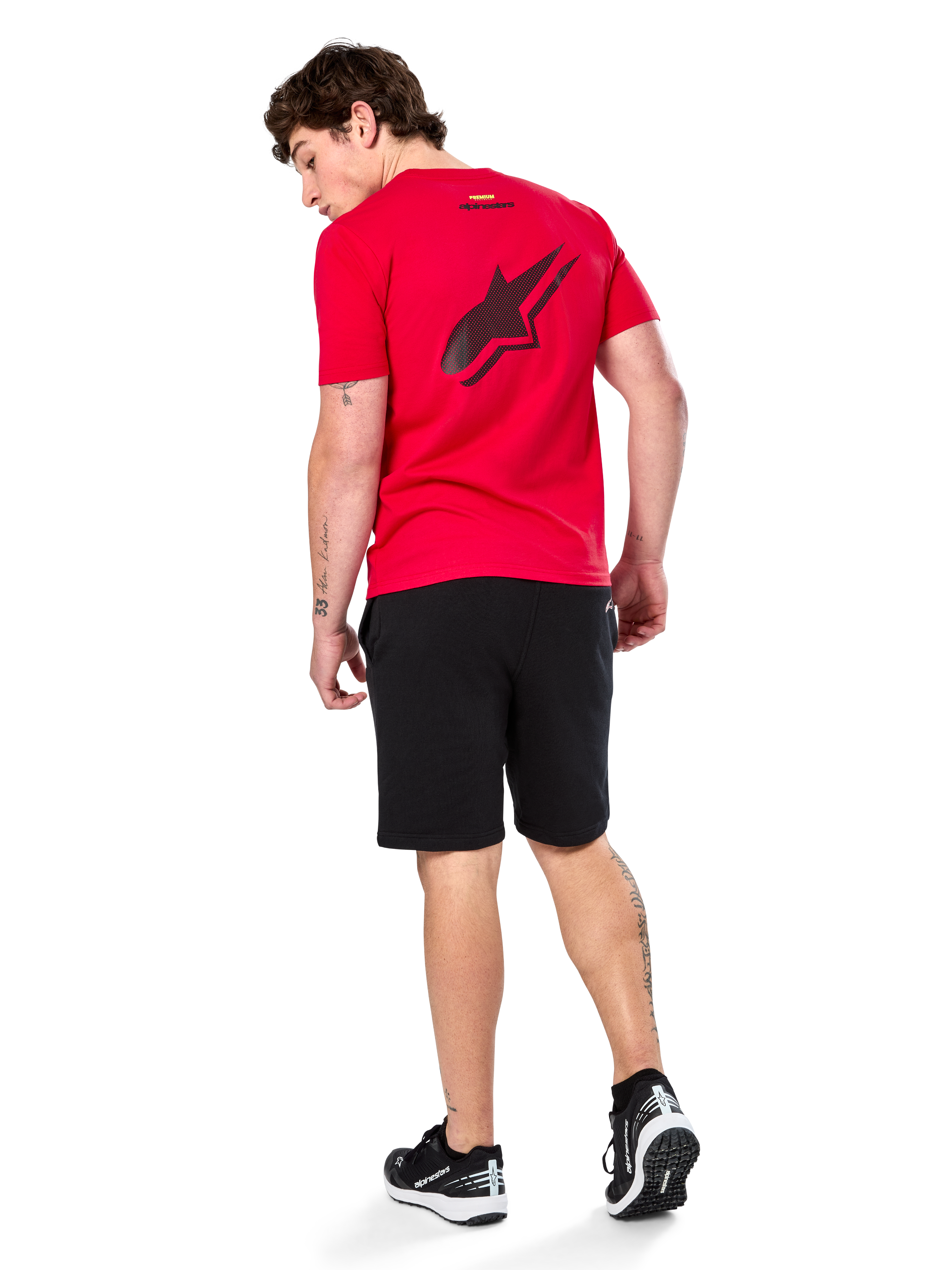 Alpinestars Formulate Csf Tee, T-shirt met korte mouwen, rood, groot zwart geperforeerd Astars-logo op de rug, gedragen met zwarte shorts en sneakers, casual motorsport-geïnspireerde streetwear