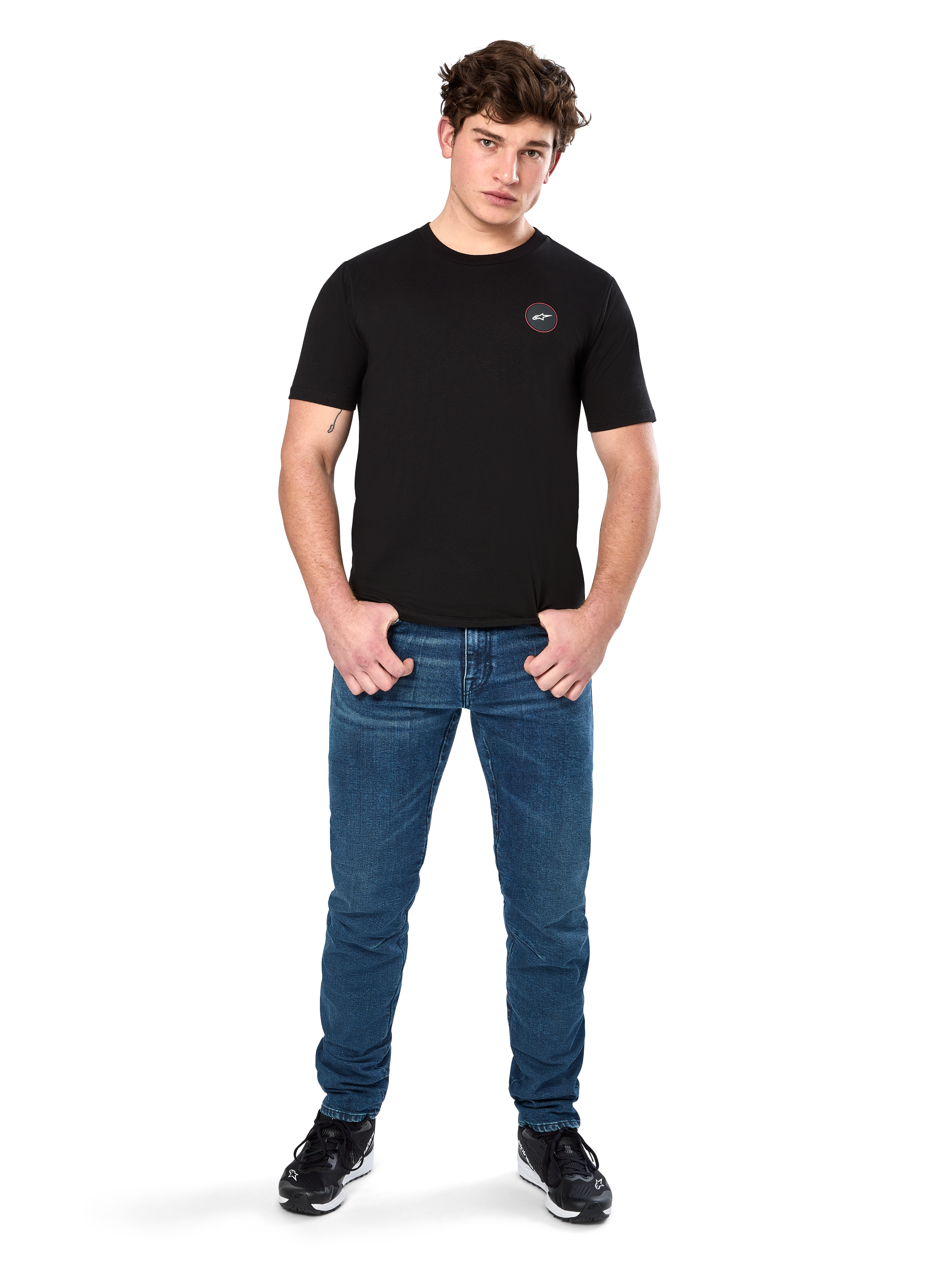 Alpinestars Dot Carbon CSF Tee, T-shirt met korte mouwen, zwart, klein rond Astars Dot-logo op de borst, gedragen met blauwe jeans en zwarte sneakers, casual motorsport streetwear