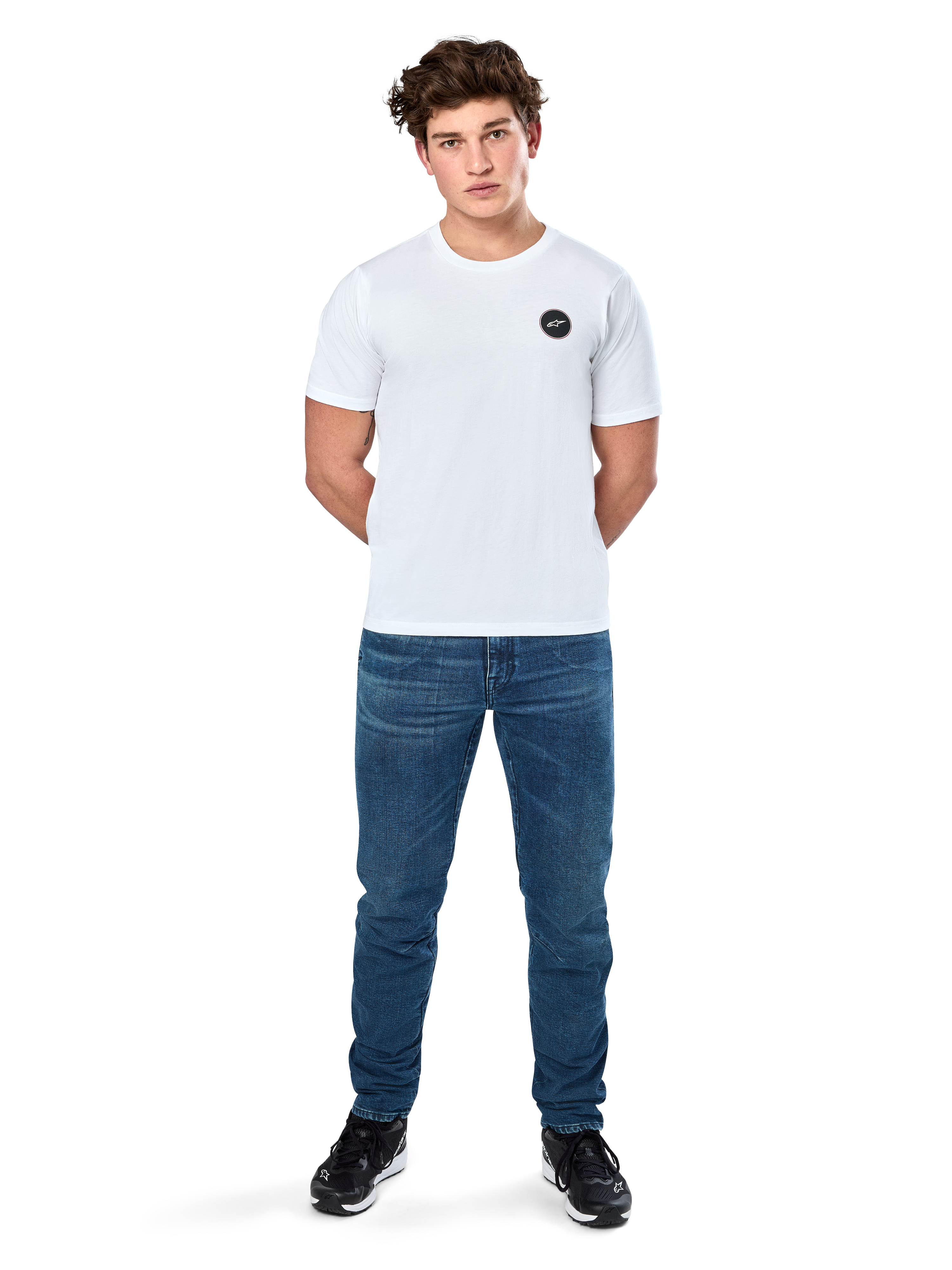 Alpinestars Dot Carbon Csf Tee, T-shirt met korte mouwen, wit, rond Astars-logo met carbon fiber look, casual motorsport streetwear, gedragen door een mannelijk model met blauwe jeans en zwarte sneakers