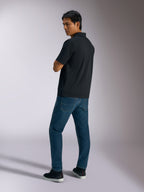 Alpinestars Impetus Sport Polo, Black, short-sleeve polo shirt with mock mesh texture and three-button placket, worn by a model with blue jeans and black sneakers, casual motorsport-inspired streetwear