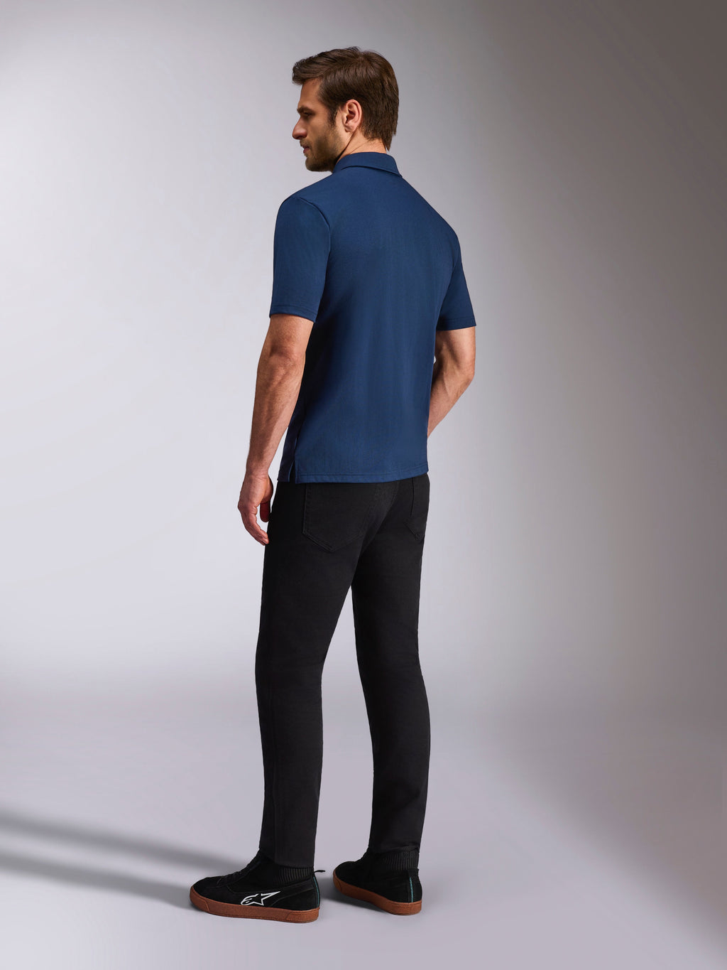 Alpinestars Impetus Sport Polo, donkerblauwe polo met korte mouwen, achter- en zij-aanzicht op model, gecombineerd met een zwarte broek en zwarte sneakers, casual motorsport lifestyle sportkleding