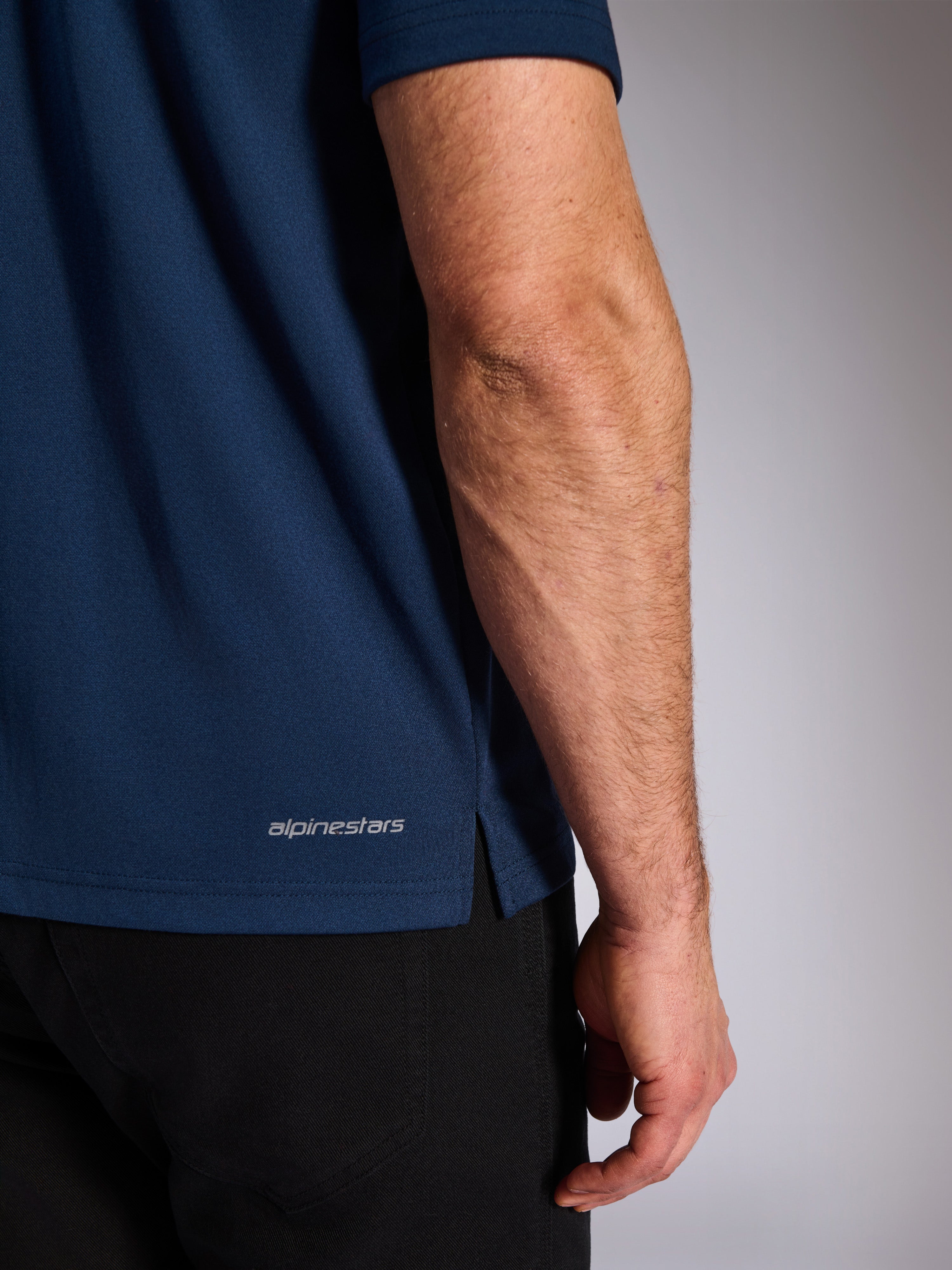 Alpinestars Impetus Sport Polo, Navy, close-up van de onderste zoom met het Alpinestars-woordmerk en zijsplit, mock-mesh gebreide textuur, casual motorsport sportkleding