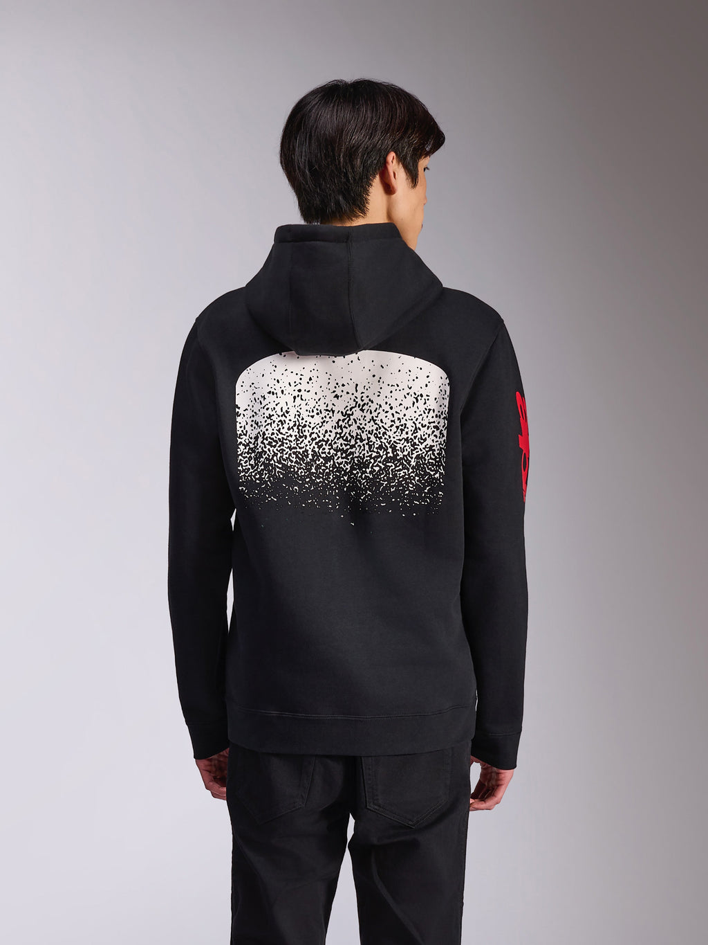 Alpinestars Obsessed Hoodie, achteraanzicht van zwarte pullover fleece hoodie, voorzien van een grote witte gespikkelde MX-verloopgraphic op de rug en rode Alpinestars-woordlogo's op de mouwen, casual streetwear geïnspireerd op de motorsport