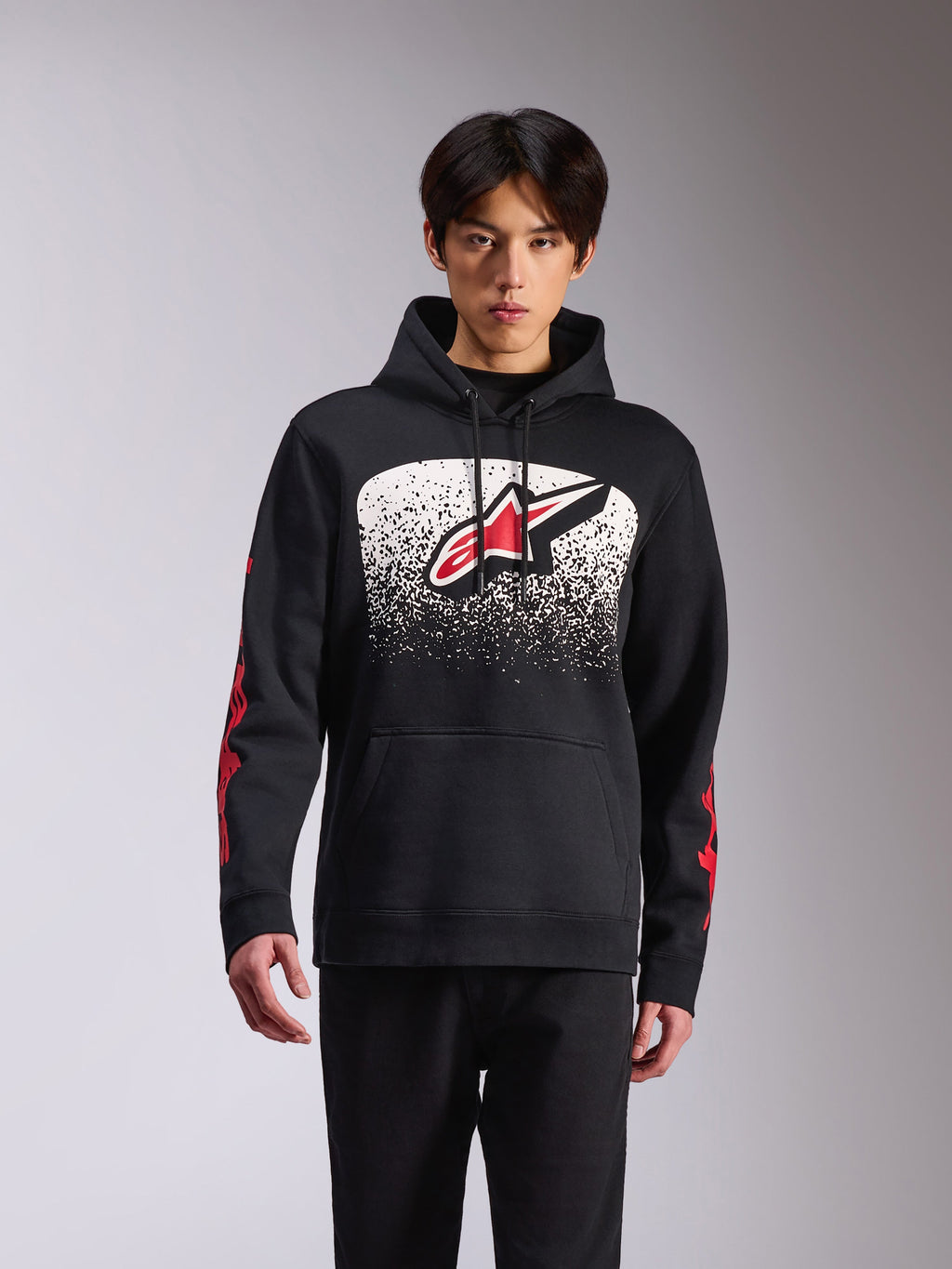 Alpinestars Obsessed Hoodie, casual sportkleding, zwarte pullover met een groot Astars-logo op de voorkant met een wit en zwart gespikkeld MX-verloop, rode branding op de mouwen, capuchon met trekkoord en geribde manchetten.