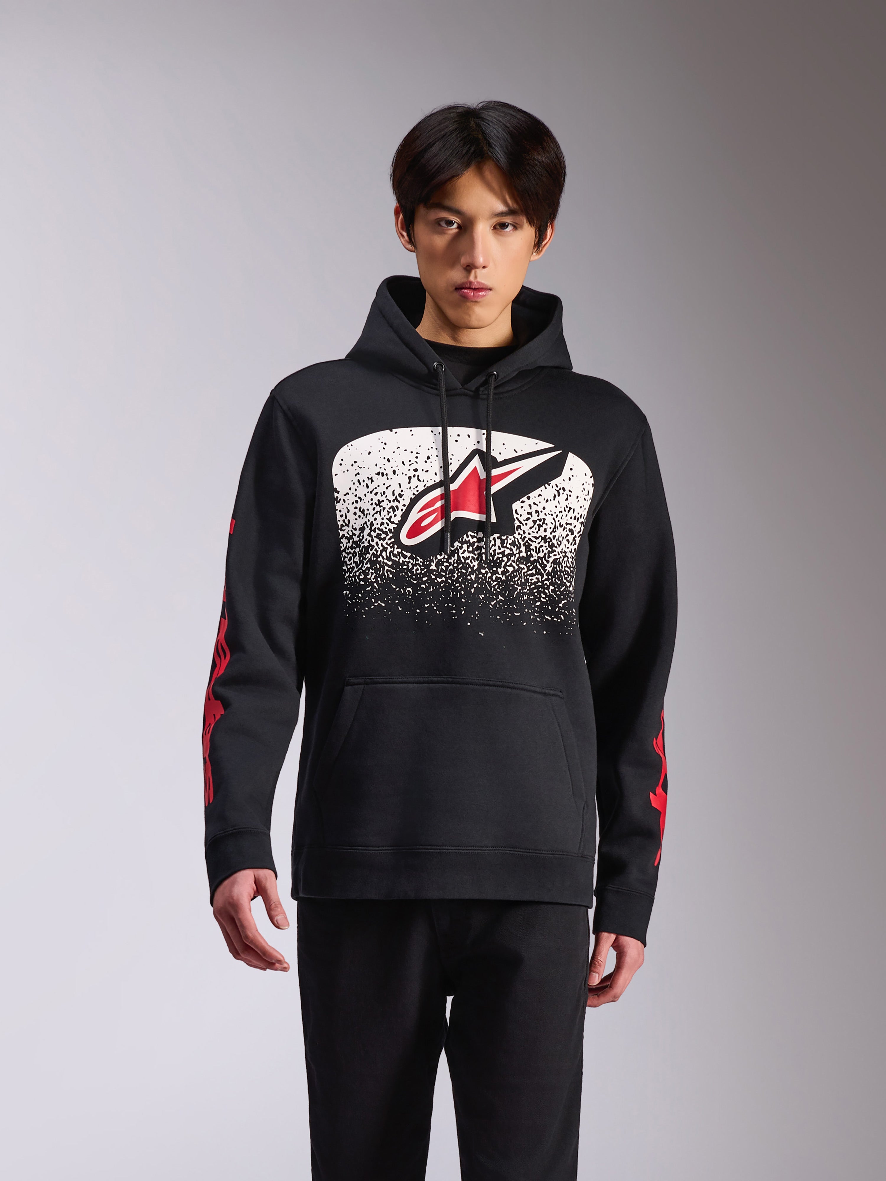 Alpinestars Obsessed Hoodie, casual sportkleding, zwarte pullover met een groot Astars-logo op de voorkant met een wit en zwart gespikkeld MX-verloop, rode branding op de mouwen, capuchon met trekkoord en geribde manchetten.