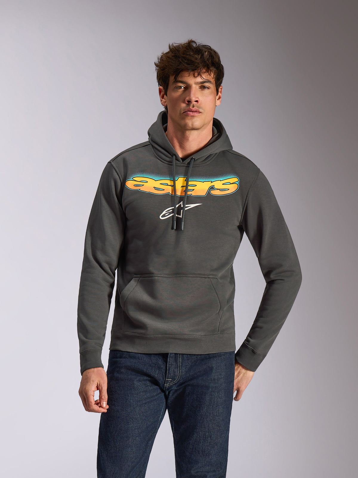 Alpinestars Ellipsoid Hoodie, casual sportkleding, gunmetal grijs met geel en blauw kleurverloop Astars-tekst en wit logo, pullover model met capuchon en trekkoord, gedragen met een donkerblauwe jeans