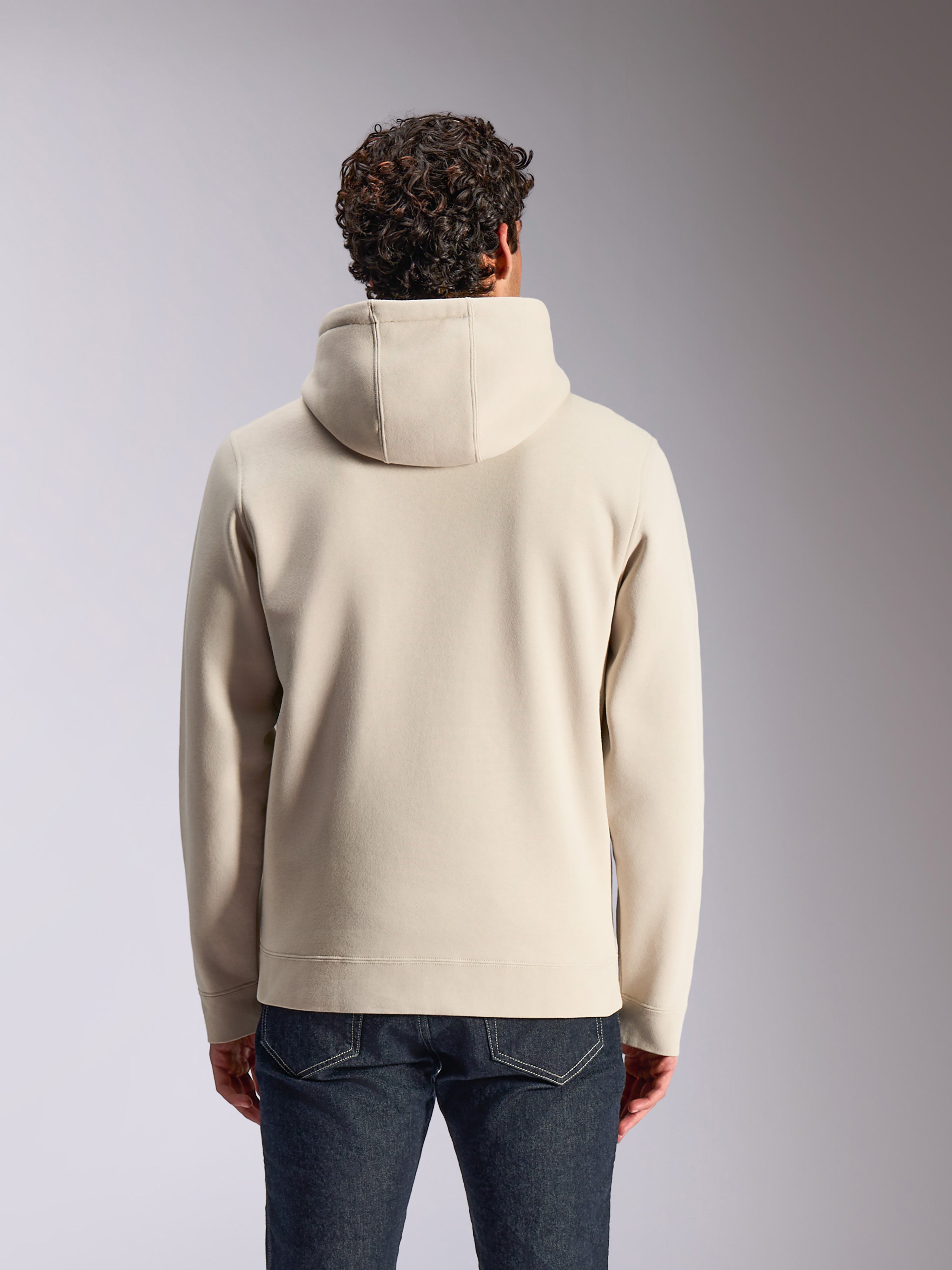 Alpinestars Pulse Hoodie, zandkleur, achteraanzicht van een mannelijk model dat de effen pullover met capuchon draagt, gecombineerd met een donkere denim jeans, casual motorsportgeïnspireerde streetwear