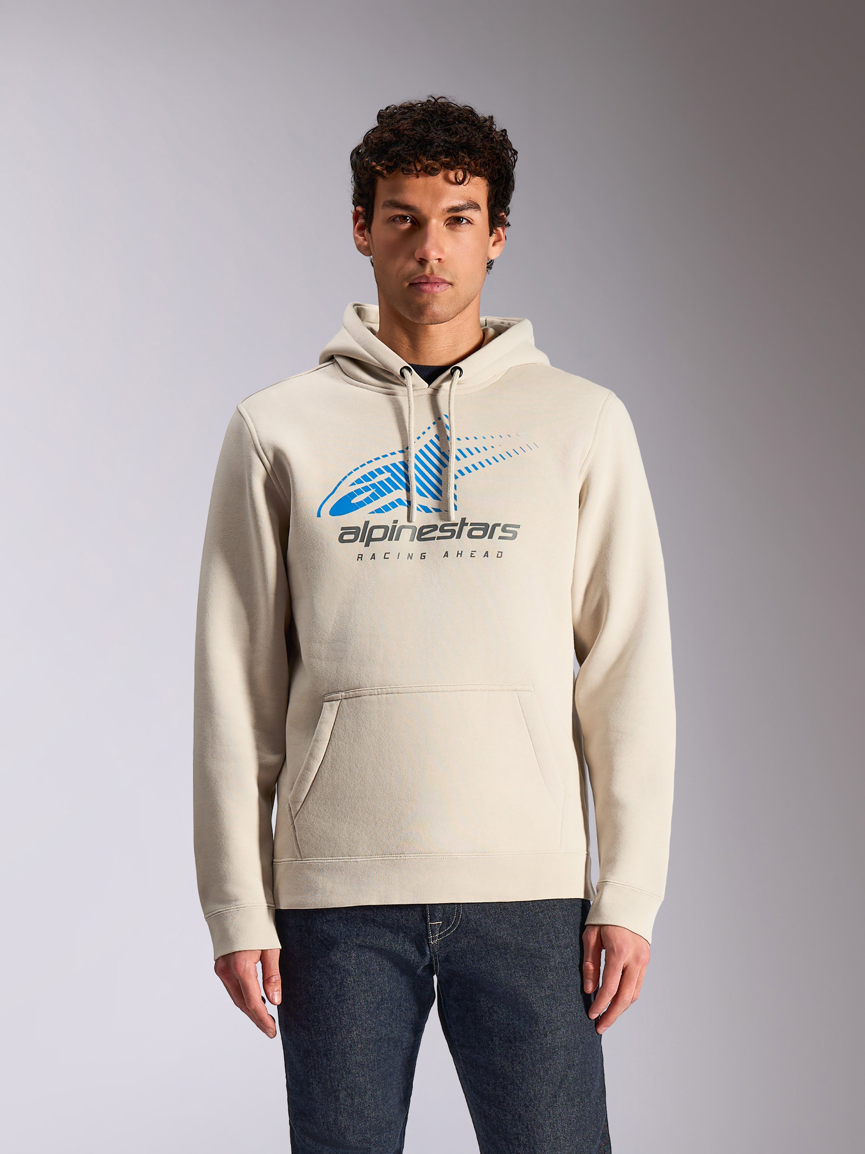 Alpinestars Pulse Hoodie, gebroken witte casual pullover hoodie, blauw en grijs Astars Combo Logo op de borst met speed line fade graphic, kangoeroezak aan de voorzijde, gedragen door model met donkere jeans, motorsport-geïnspireerde streetwear