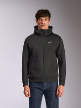Alpinestars Cypher Hoodie, zwarte fleece hoodie met ritssluiting aan de voorzijde, voorzien van een hoge capuchon met witte branding en een klein wit Astars-logo op de borst, gedragen door een model met blauwe jeans, casual op motorsport geïnspireerde streetwear.