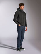 Alpinestars Cypher Hoodie, casual streetwear, zwarte hoodie met rits, mannelijk model met donkerblauwe jeans en zwarte sneakers, hoge capuchon met Alpinestars-woordlogo, klein wit Astars-logo op de borst, strakke motorsport-geïnspireerde lifestyle-look