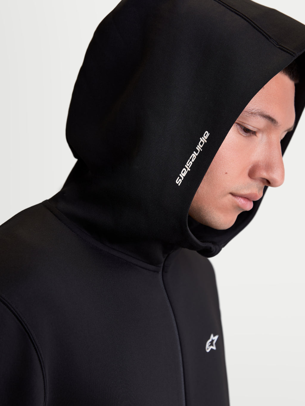 Alpinestars Cypher hoodie, heren fleecehoodie met rits, zwart, close-up van de hoge capuchon met wit Alpinestars-woordlogo en technische tri-blend fleece.