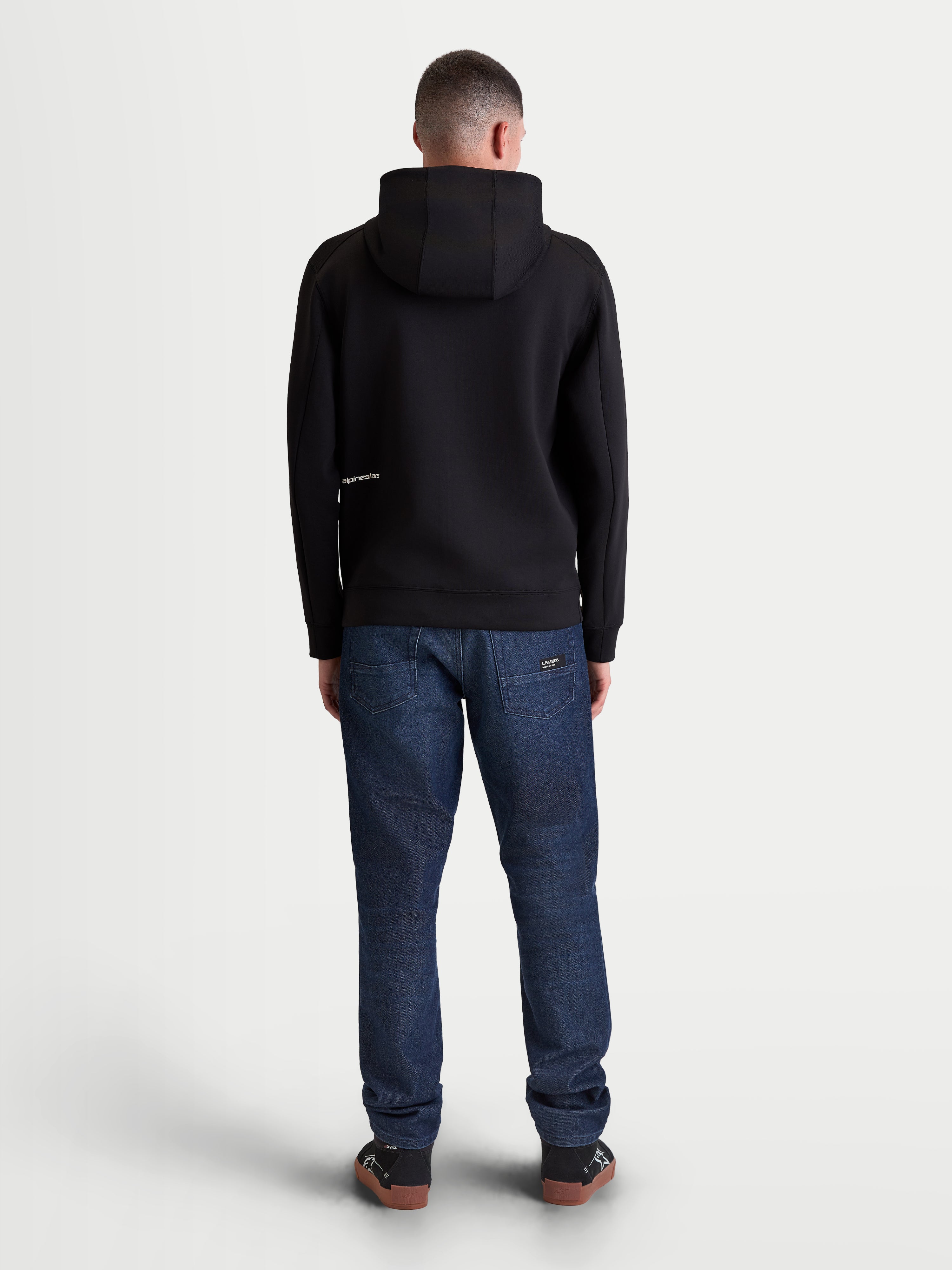 Alpinestars Cypher Hoodie, premium zwarte fleecehoodie met rits, achteraanzicht op model met hoge capuchon en minimalistisch logodetail, tri-blend performance stof, unisex casual sportswear en motorsports lifestyle.