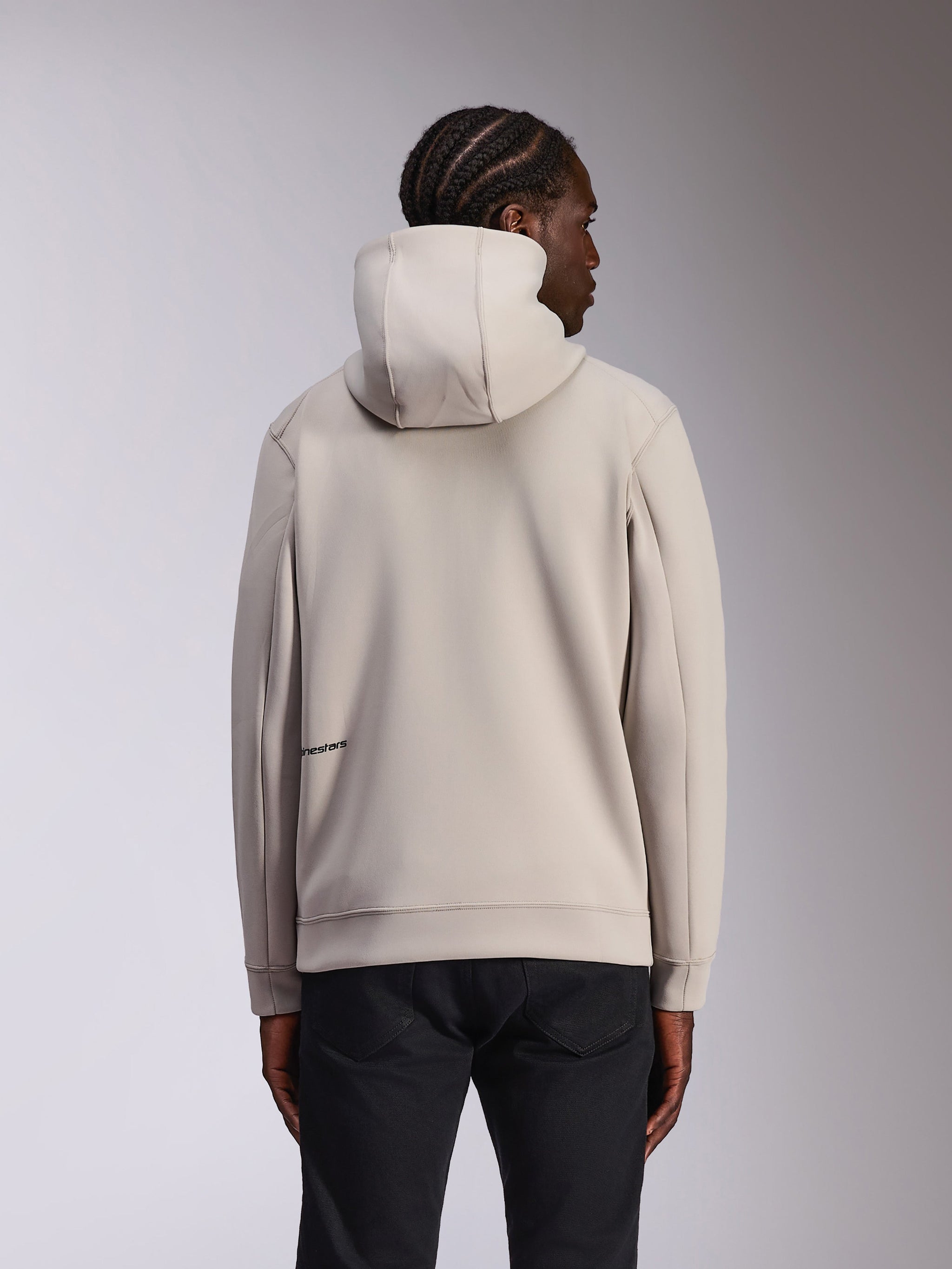 Alpinestars Cypher Hoodie, casual sportkleding, Cement grijs, achteraanzicht op model, hoge capuchon, dubbelzijdig fleece materiaal, minimaal Alpinestars-logo op de onderrug, gecombineerd met een zwarte broek