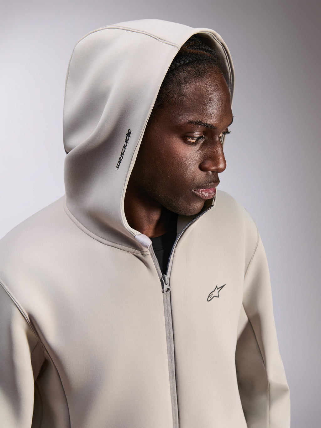 Alpinestars Cypher Hoodie, fleece hoodie met rits, Cementgrijs, gedragen met de capuchon op, voorzien van Alpinestars-woordlogo op de capuchon en klein Astars-logo op de borst, casual motorsport-geïnspireerde streetwear