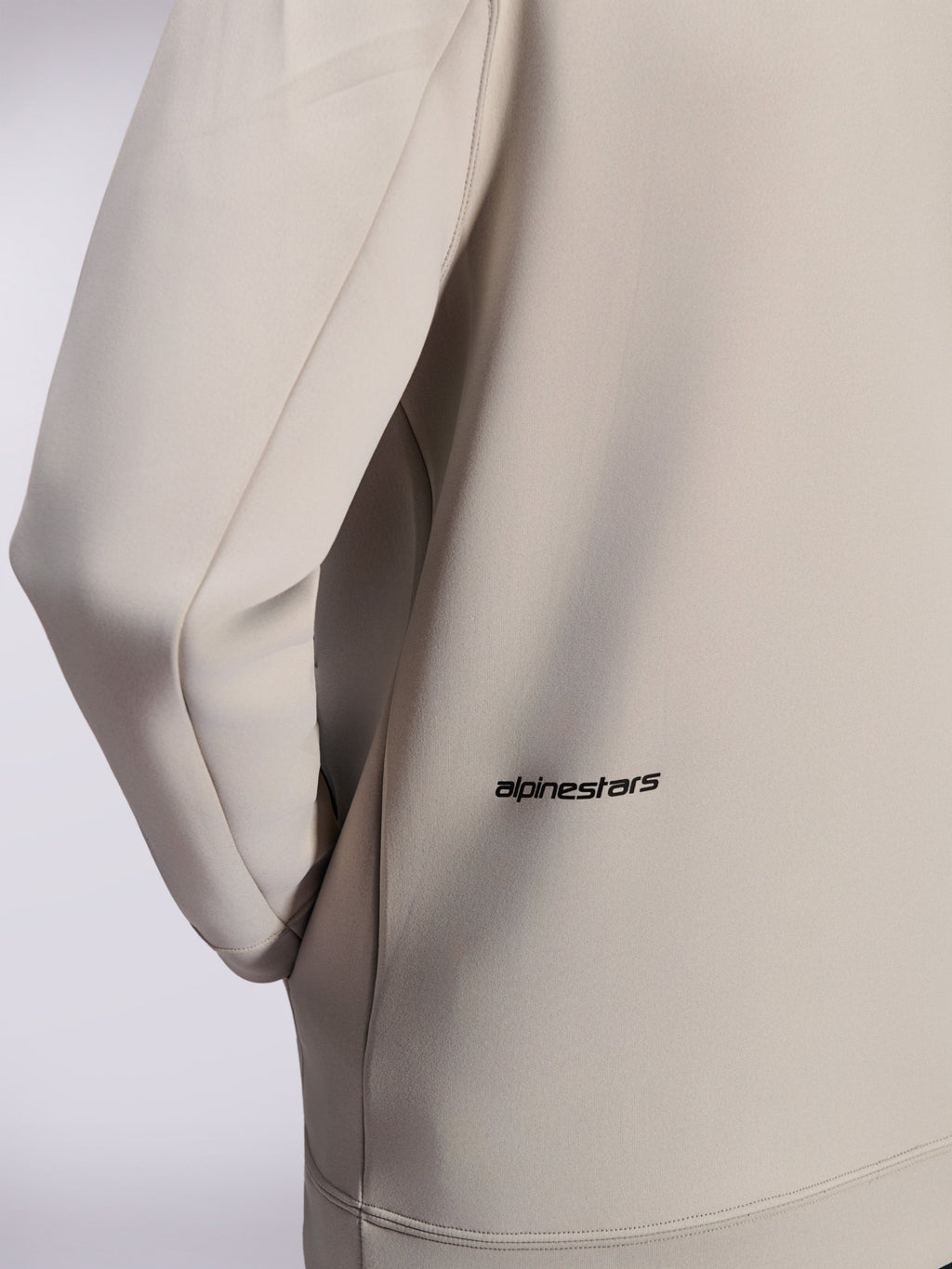 Alpinestars Cypher Hoodie, dubbelzijdige fleece hoodie met rits, Cementgrijs, close-up van klein zwart Alpinestars woordlogo op de onderrug, detail van zak in de zijnaad en gladde textuur van de stof
