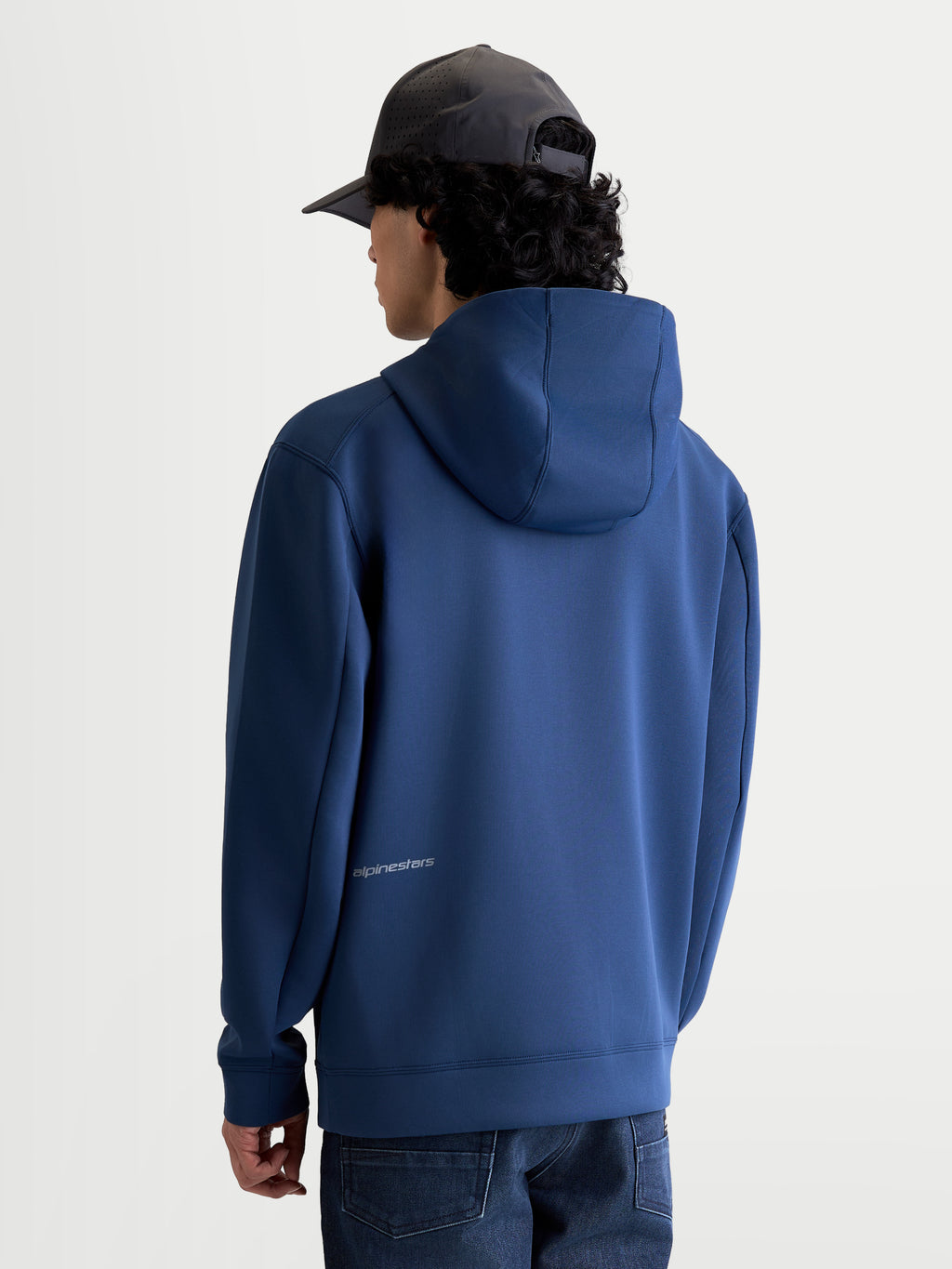 Alpinestars Cypher Hoodie, sportieve fleece-hoodie met rits, achteraanzicht op model, staalblauw, tri-blend materiaal, capuchon met hoge hals en meshvoering, subtiel Alpinestars-logo op de onderrug, casual motorsportstijl.