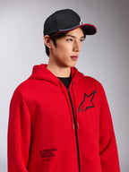 Alpinestars Transverse Hoodie, Red zip-front fleece, black Astars logo on chest and 'One Goal. One Vision.' text on the lower front, casual motorsport streetwear, worn by a model with a black cap