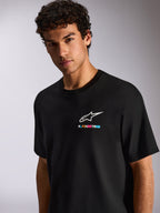 A man wearing the Alpinestars Wild Oversized CSF Tee, Black Short Sleeve T-Shirt, featuring a white Astars logo and vibrant multi-colored branding on the chest, casual motorsport streetwear