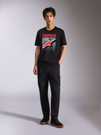Alpinestars Noka CSF Tee, T-shirt met korte mouwen, zwart, Astars-logo op de voorzijde met rood-witte MX-verloopgrafiek, gedragen door een model met zwarte cargobroek, casual motorsport streetwear